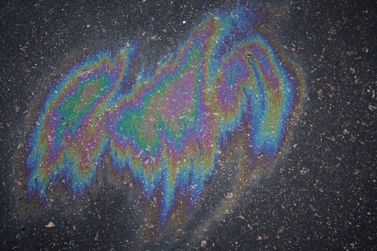 Gasoline or oil spill on asphalt creating rainbow sheen reflecting light.