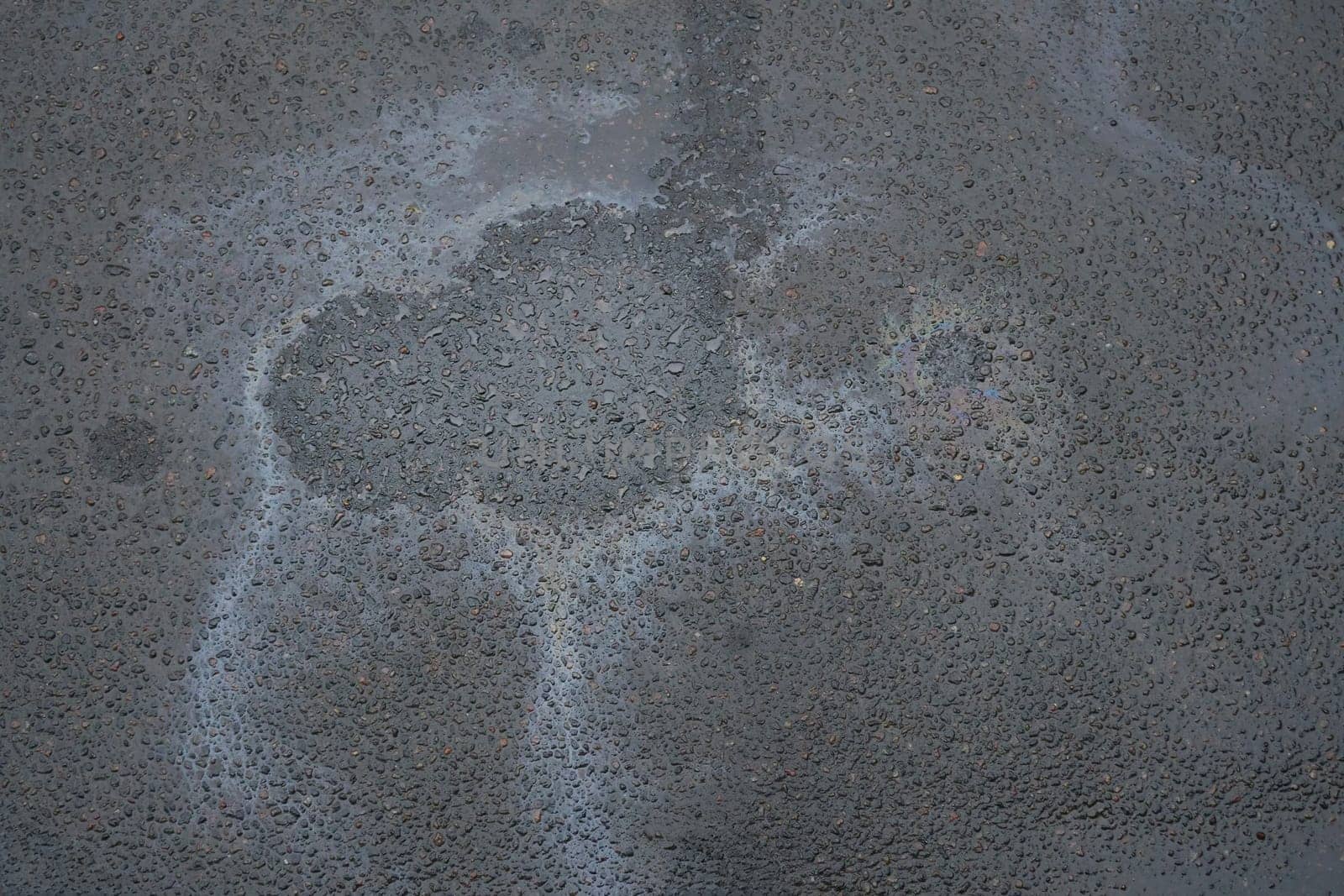 Colored texture of oil products on asphalt in bright sunlight after rain. Oil dripped from the car engine onto the road