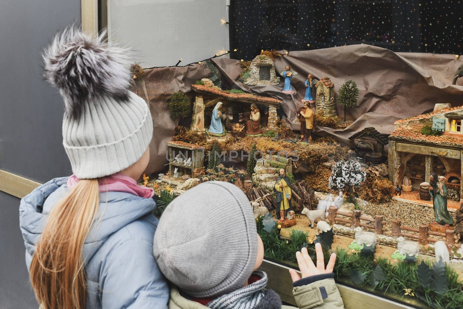 Children are looking at a Christmas nativity scene with baby Jesus Creche Figurines in a shop window