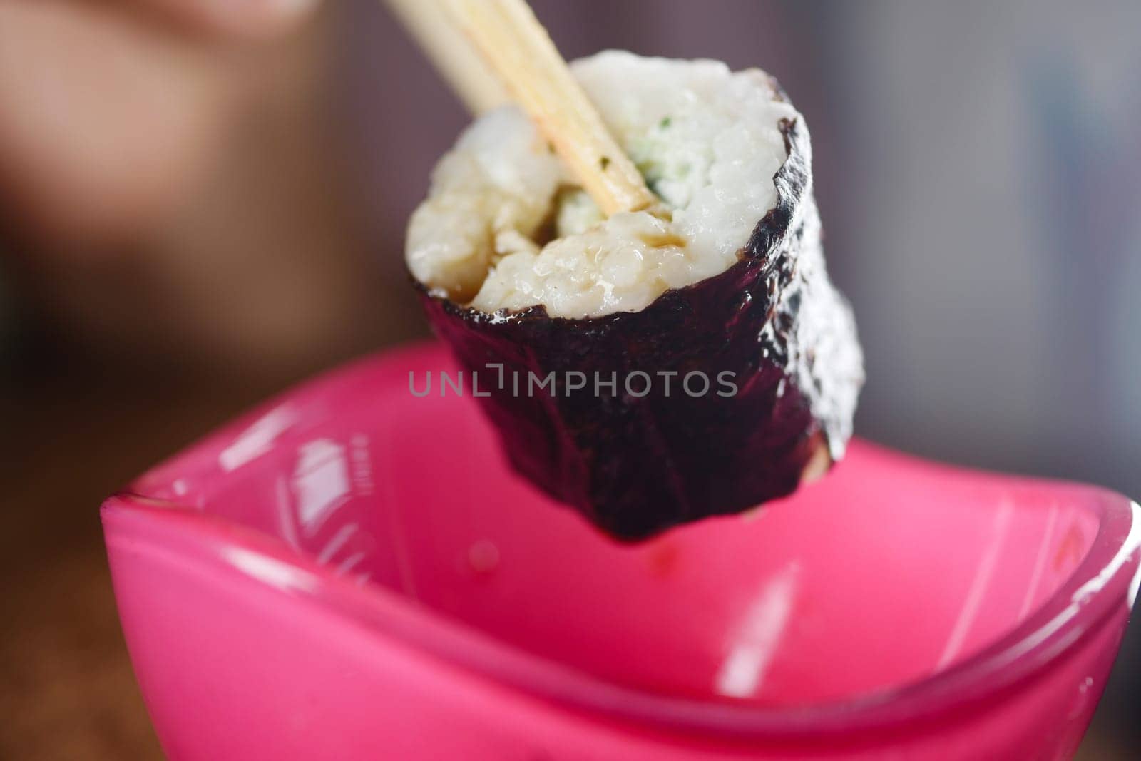 A piece of sushi, expertly held with chopsticks, is now poised for dipping into the soy sauce