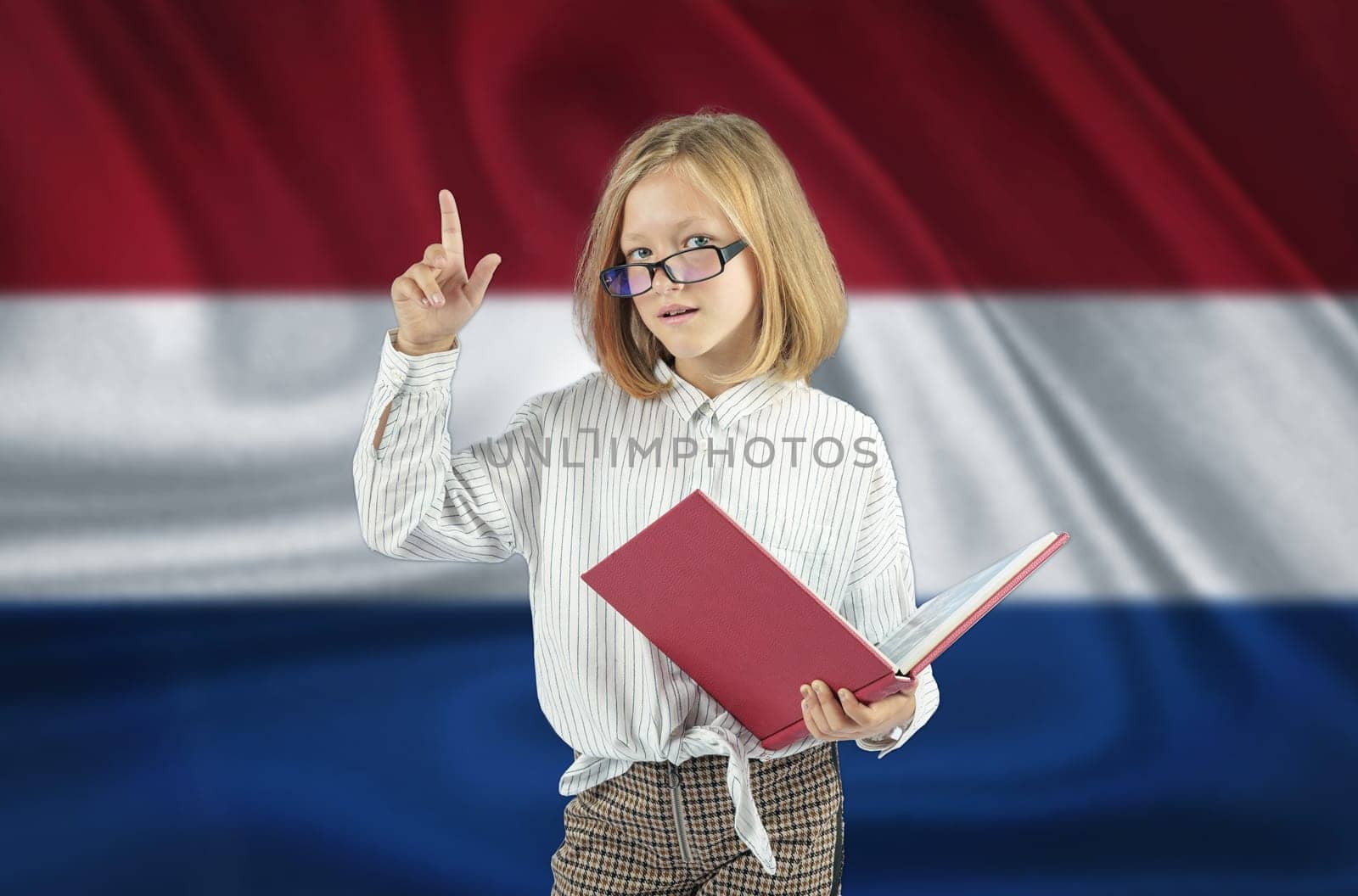 A girl with a book in her hand shows a gesture - attention on the background of the flag of Netherlands. Education concept.