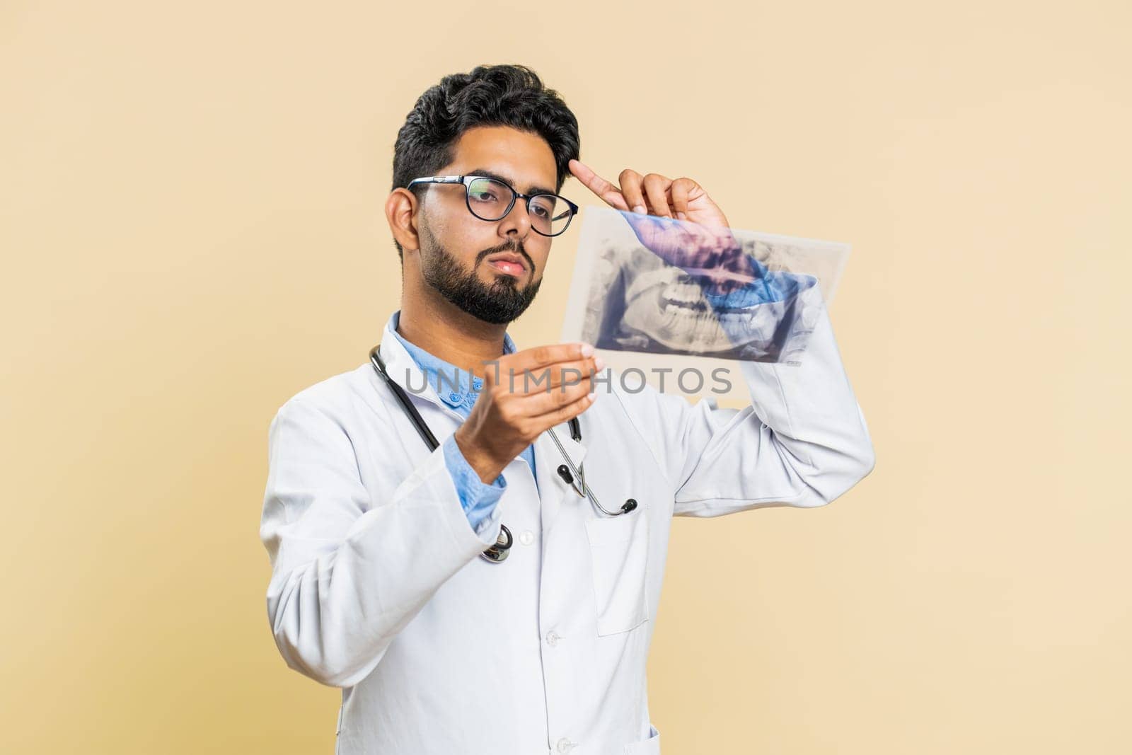 Indian young doctor orthodontist man examines a panoramic x-ray picture of the jaw teeth. 3D model of the patient's mouth, MRI scan. Dentistry, oral care. Arabian stomatology guy on beige background