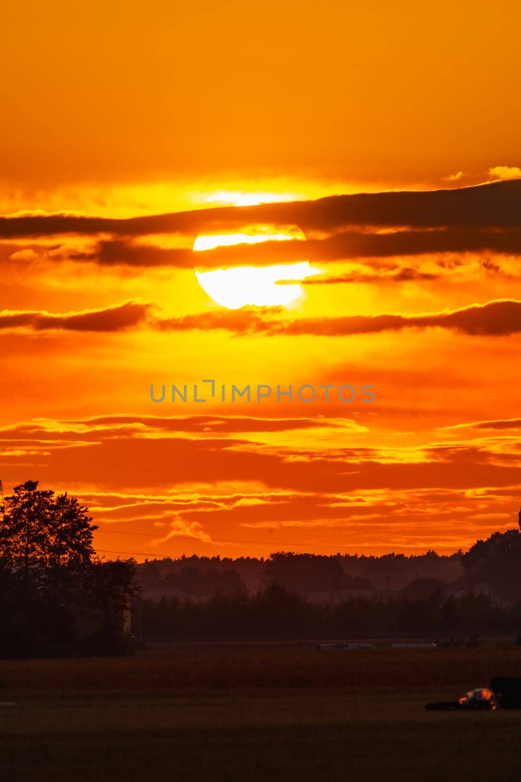 Beautiful cloudy red sunset with gigantic sun over big fields and trees seen by 600mm camera lens  by Wierzchu