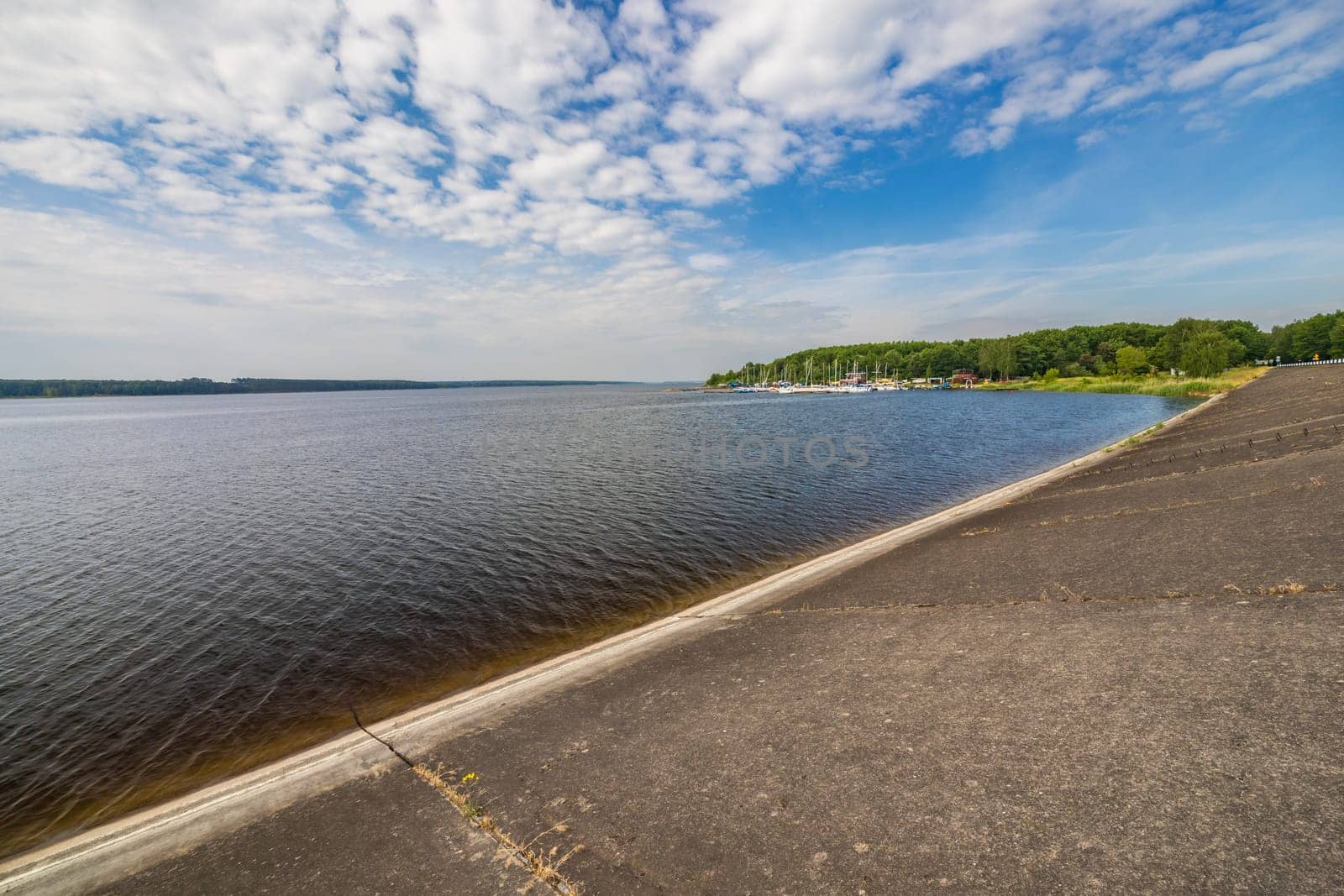 Small bay behind small local harbor at the coast of big lake next to water dame and road