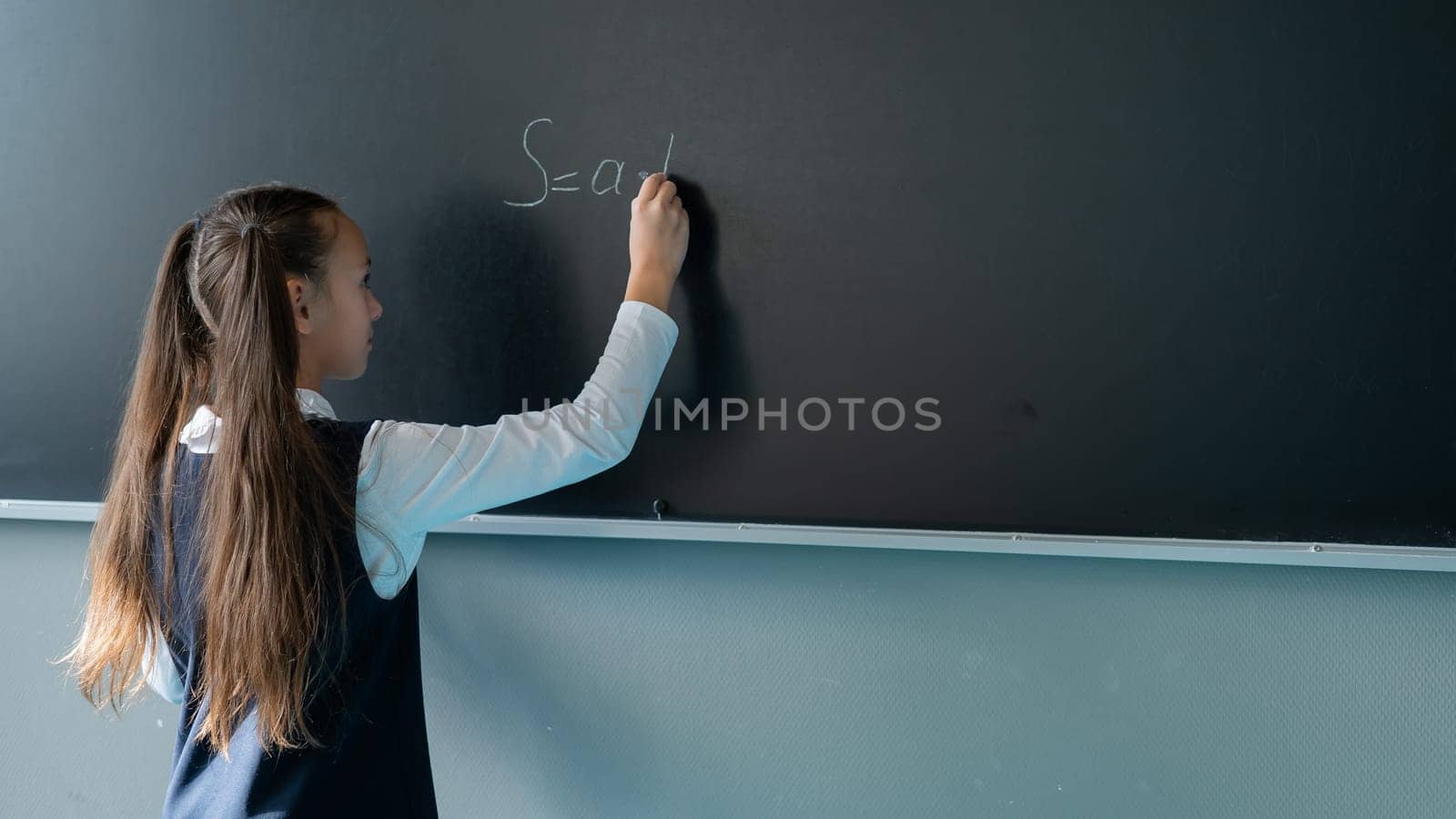 The schoolgirl answers at the lesson. Caucasian girl writes a formula on a blackboard