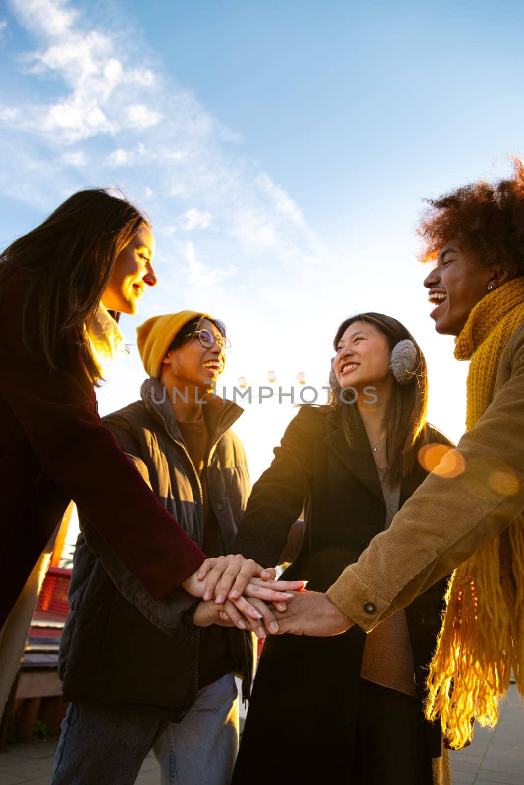 Group of multiracial college student friends stacking hands together in a circle as symbol of community and friendship outdoors on a winter day. Vertical image. Community and cooperation concepts.