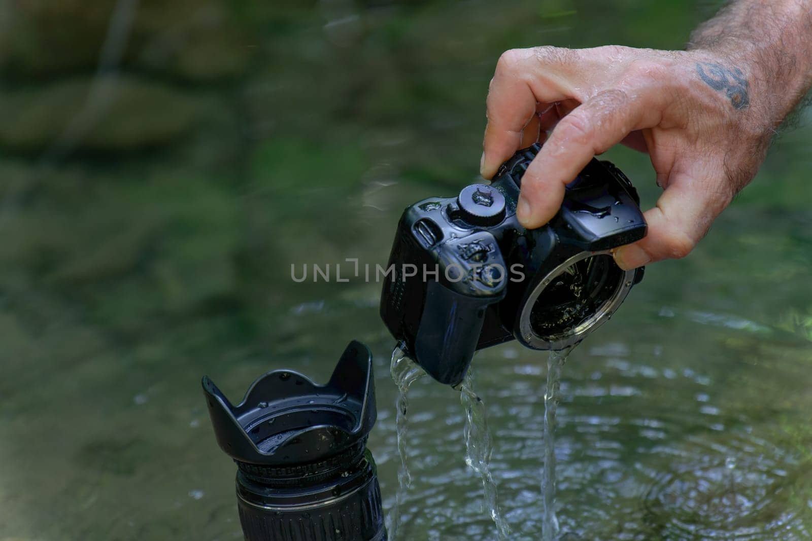 a man removes water from inside his reflex camera that has fallen into the river by joseantona