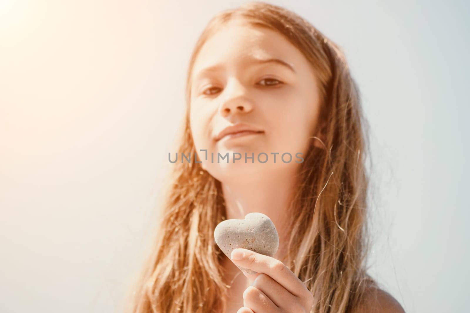 Happy girl holding in hand a stone in the shape of a heart against the background of the sea. Summer holiday vacation and travel concept. by panophotograph