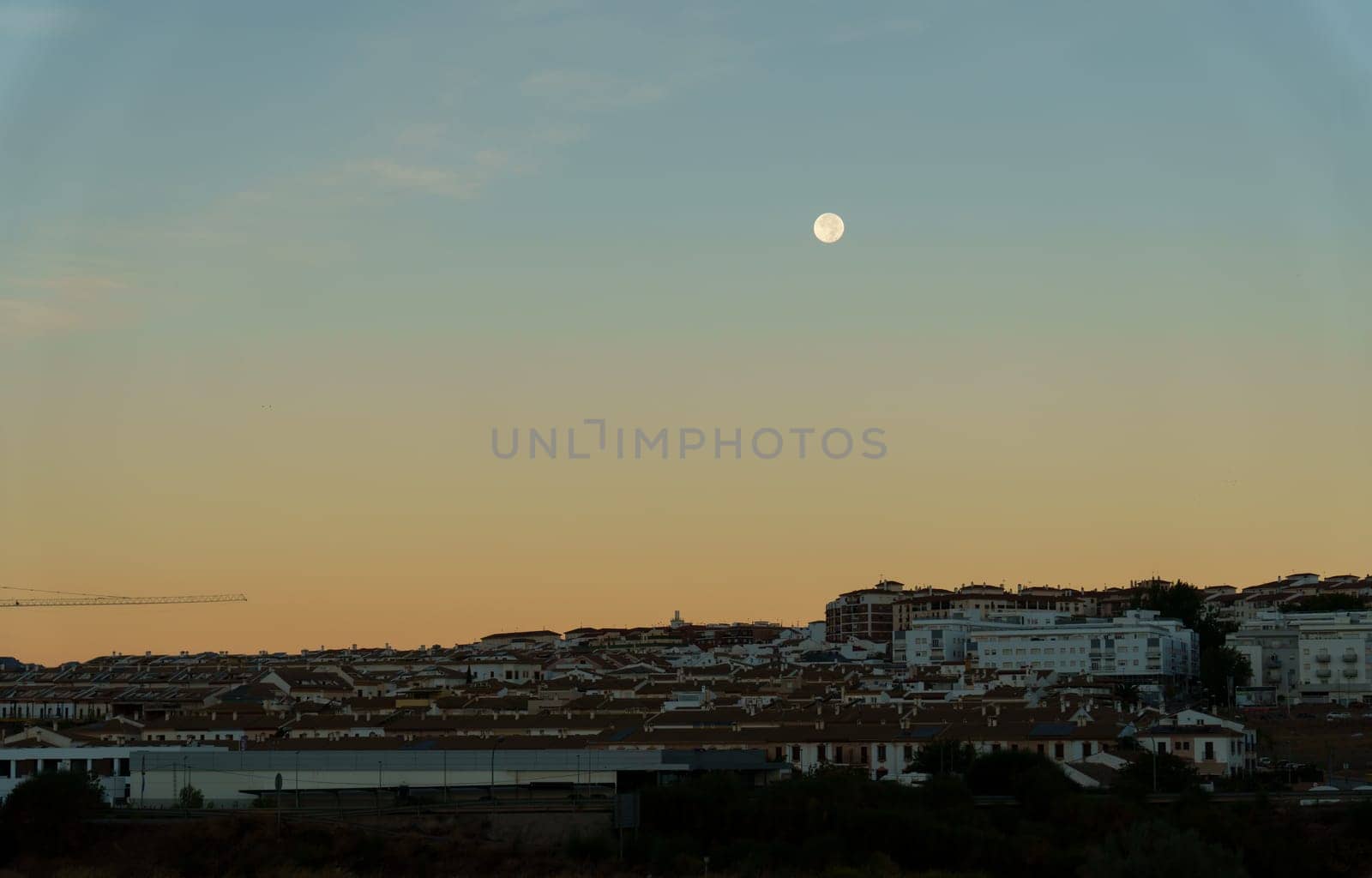 sunrise in the city with reddish and blue tones with the full moon in the sky. by joseantona