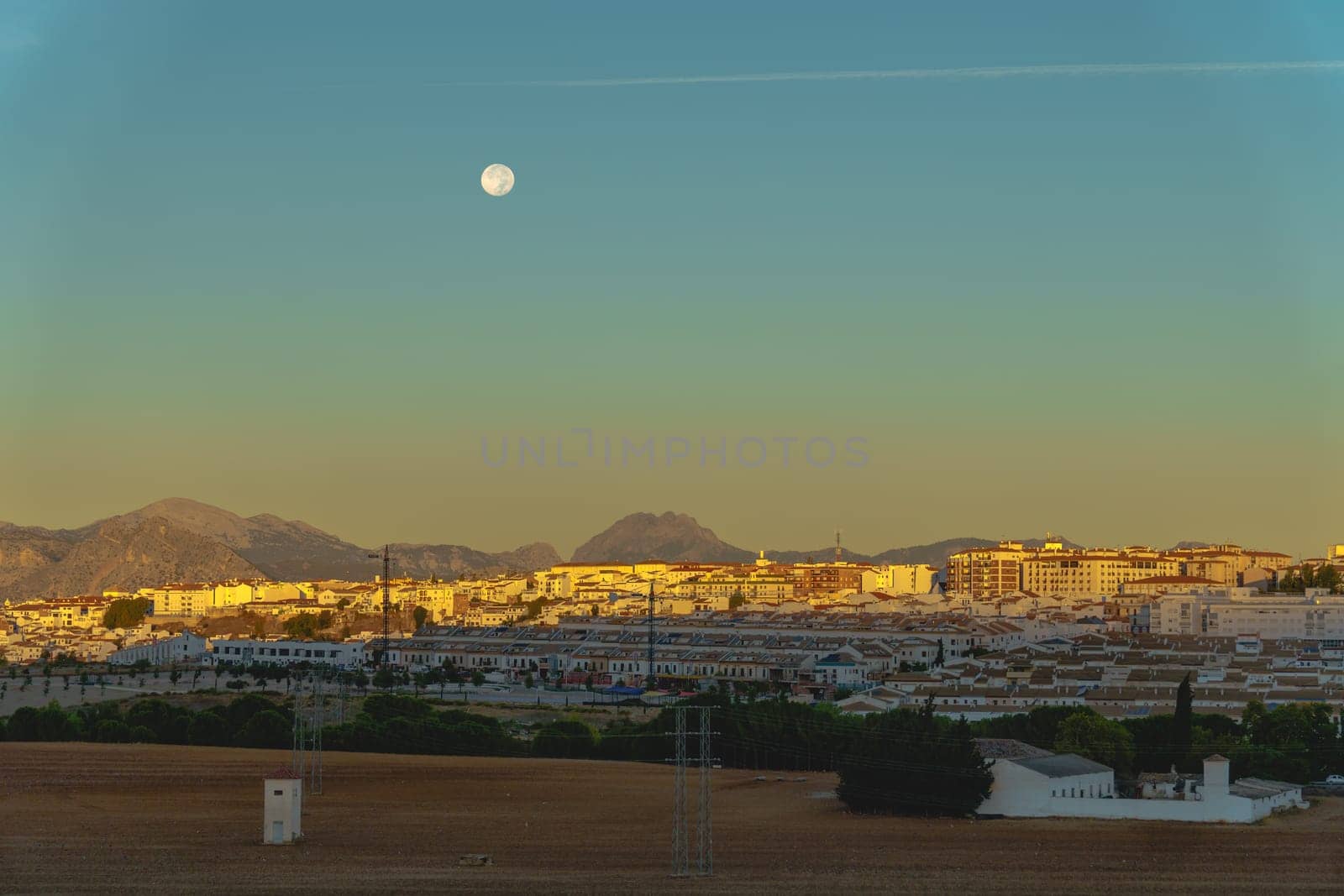 sunrise cityscape with reddish and blue tones with a full moon in the sky