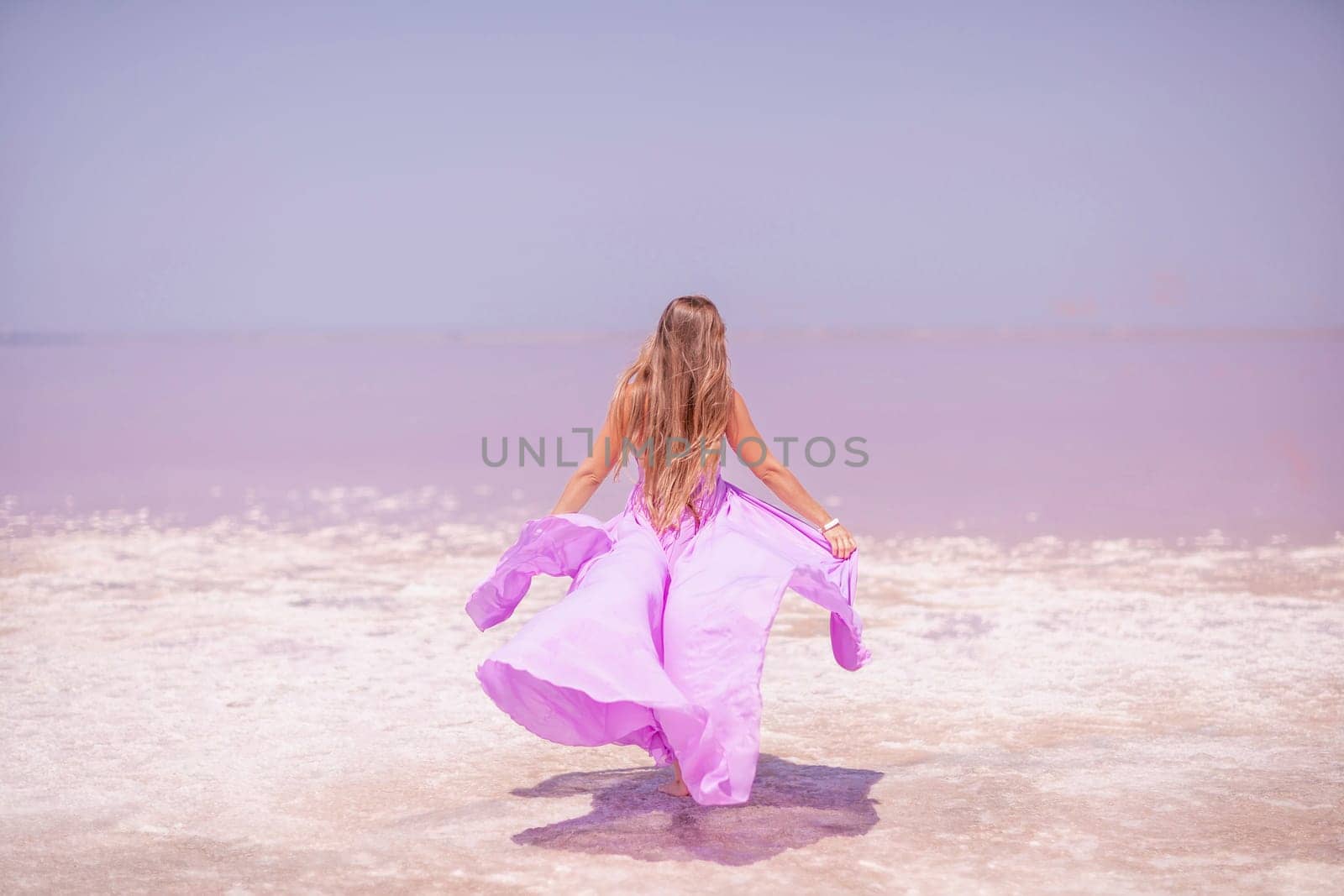 Woman pink salt lake. Against the backdrop of a pink salt lake, a woman in a long pink dress takes a leisurely stroll along the white, salty shore, capturing a wanderlust moment