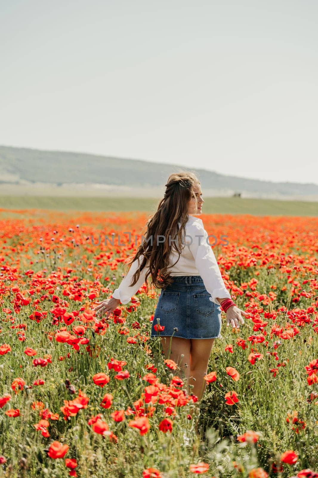 Woman poppies field. Back view of a happy woman with long hair in a poppy field and enjoying the beauty of nature in a warm summer day. by Matiunina