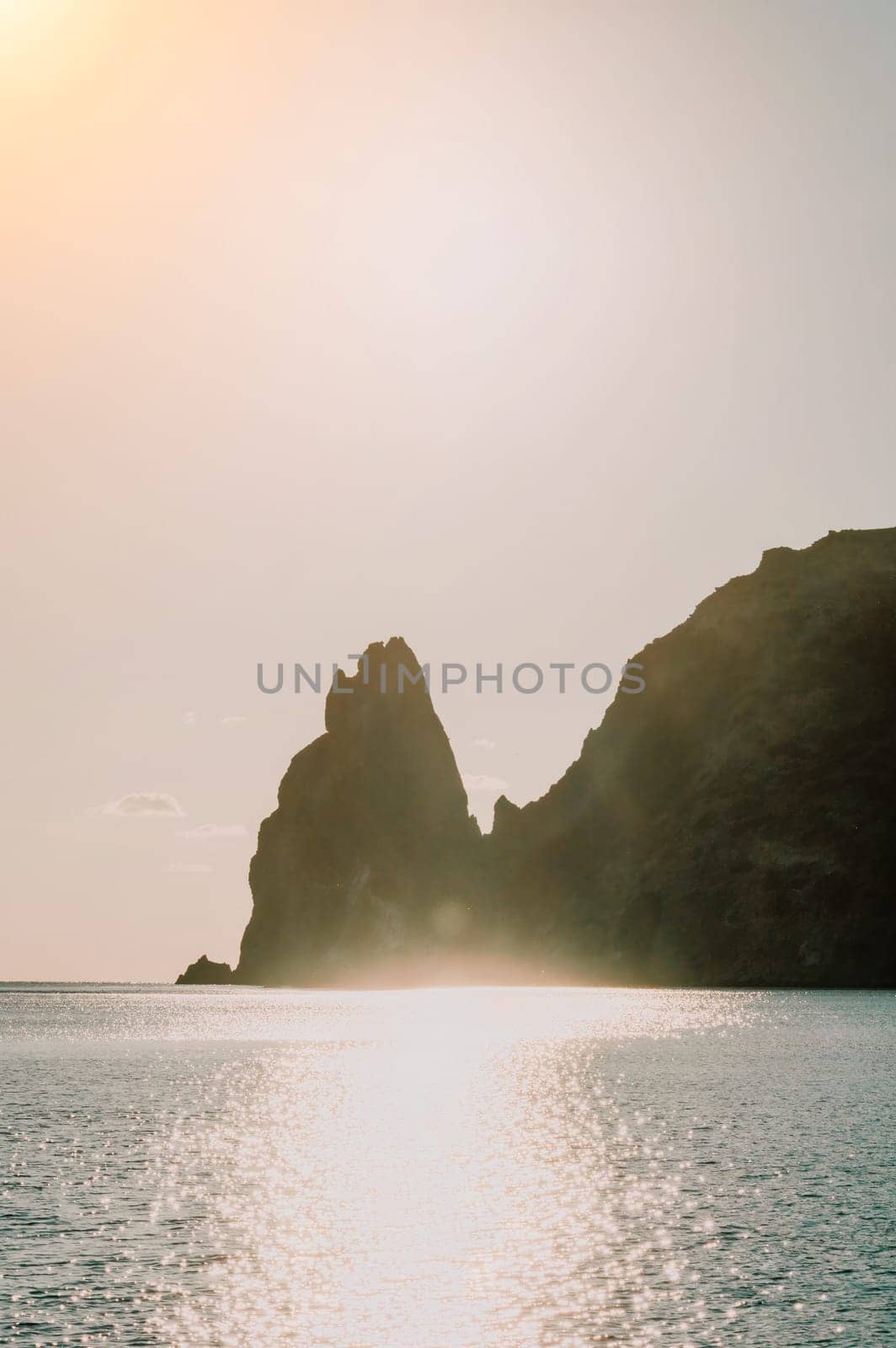 A red burning sunset over the sea with rocky volcanic cliff. Abstract nature summer ocean sea background. Small waves on golden warm water surface with bokeh lights from sun. by panophotograph