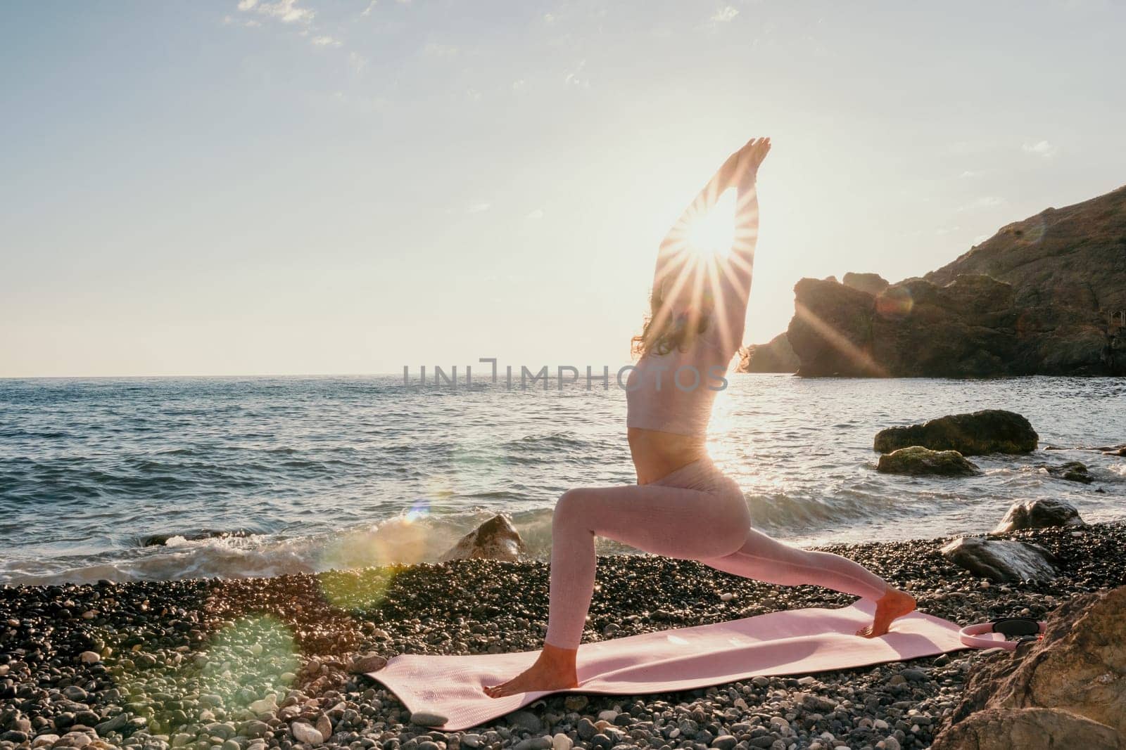 Young woman with black hair, fitness instructor in pink sports leggings and tops, doing pilates on yoga mat with magic pilates ring by the sea on the beach. Female fitness daily yoga concept