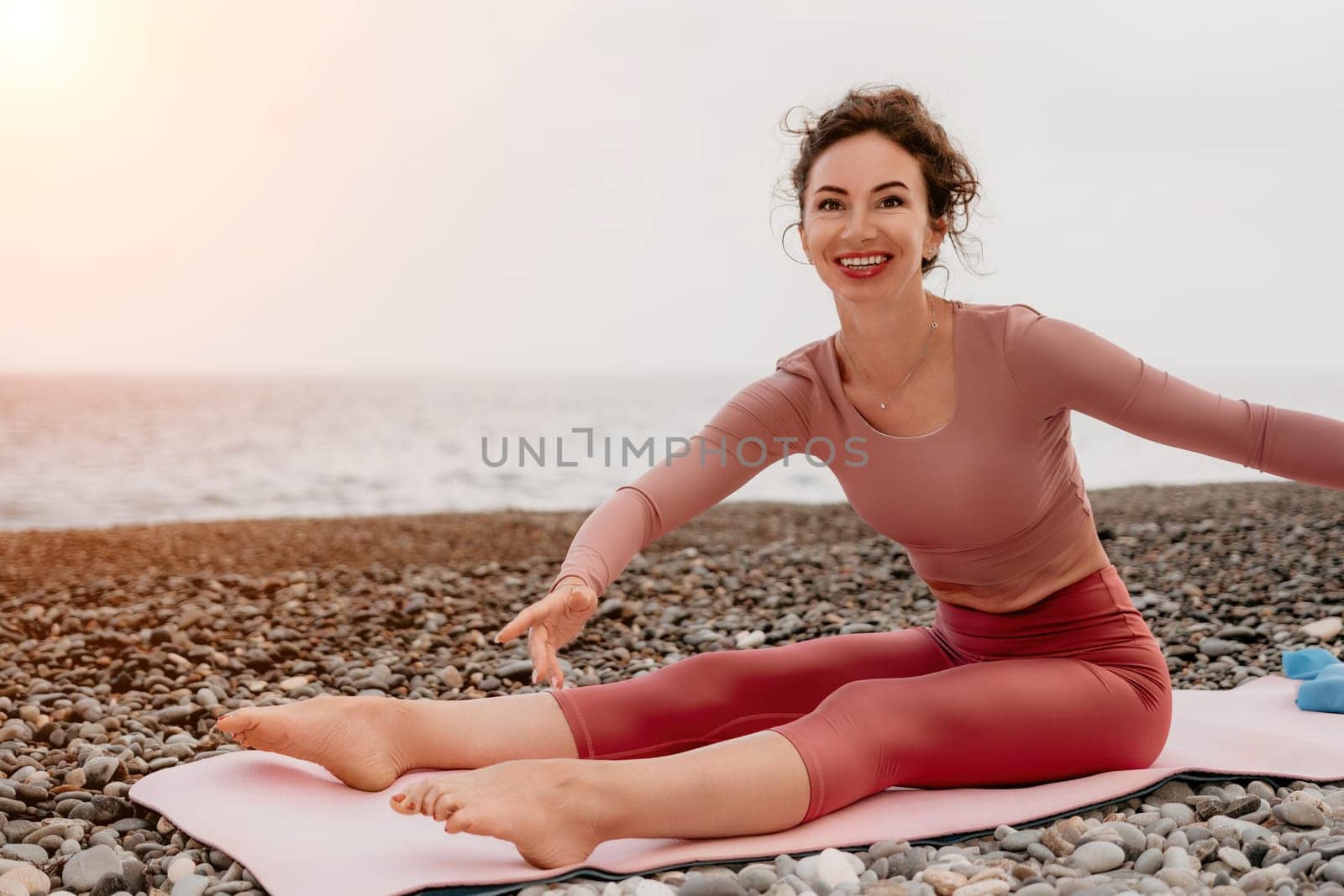 Middle aged well looking woman with black hair doing Pilates with the ring on the yoga mat near the sea on the pebble beach. Female fitness yoga concept. Healthy lifestyle, harmony and meditation.