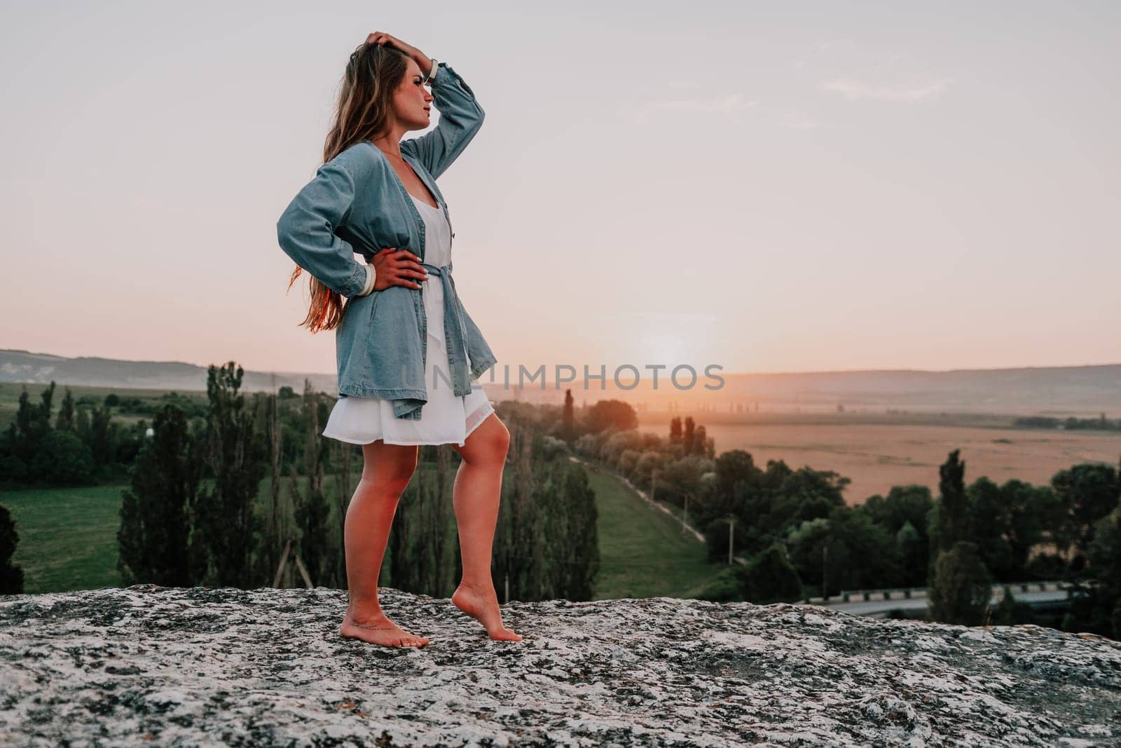 Romantic beautiful bride in white dress posing with sea and mountains in background. Stylish bride standing back on beautiful landscape of sea and mountains on sunset