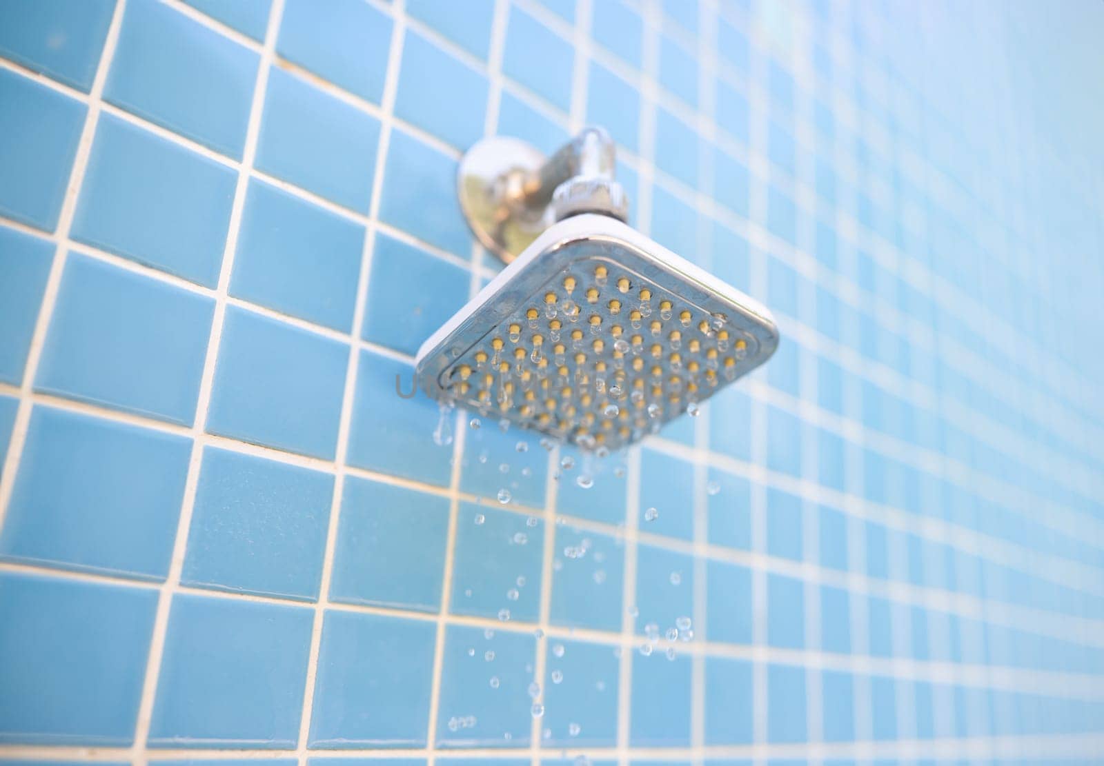 Wall-mounted outdoor shower and water drops on blue tile background. Summer showers for tourists in hotels