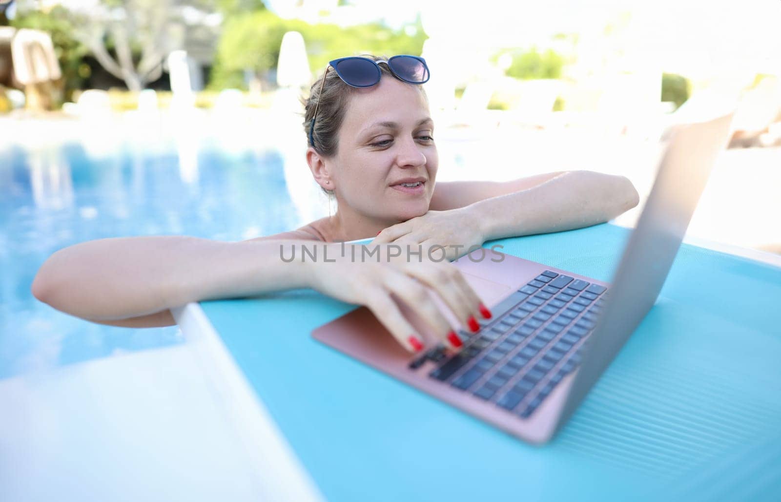 Beautiful woman in pool is typing on laptop. Telework remote work and communication with subscribers