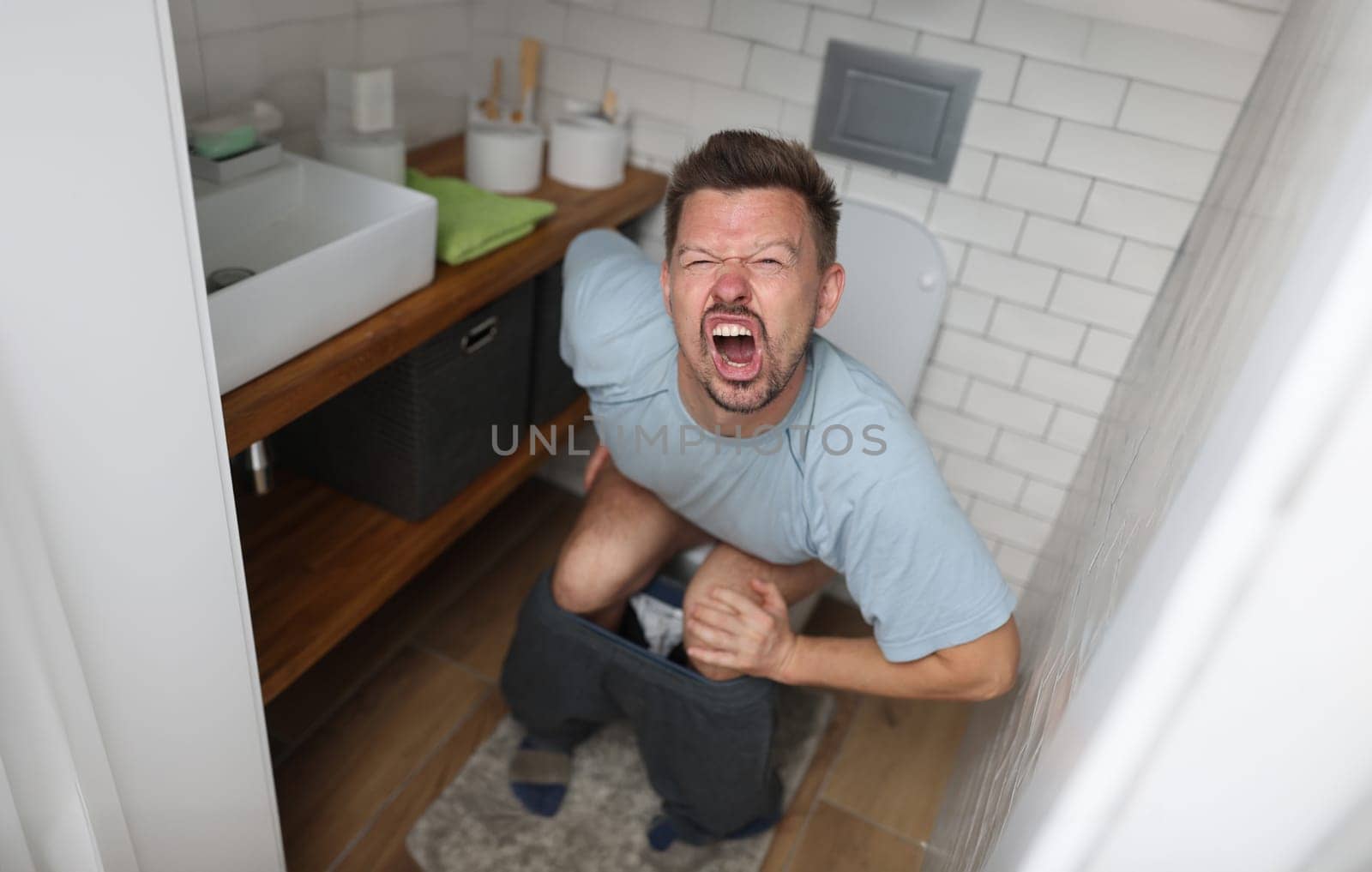 Man suffering from hemorrhoids screams on toilet in toilet. Internal hemorrhoids causes symptoms and treatment