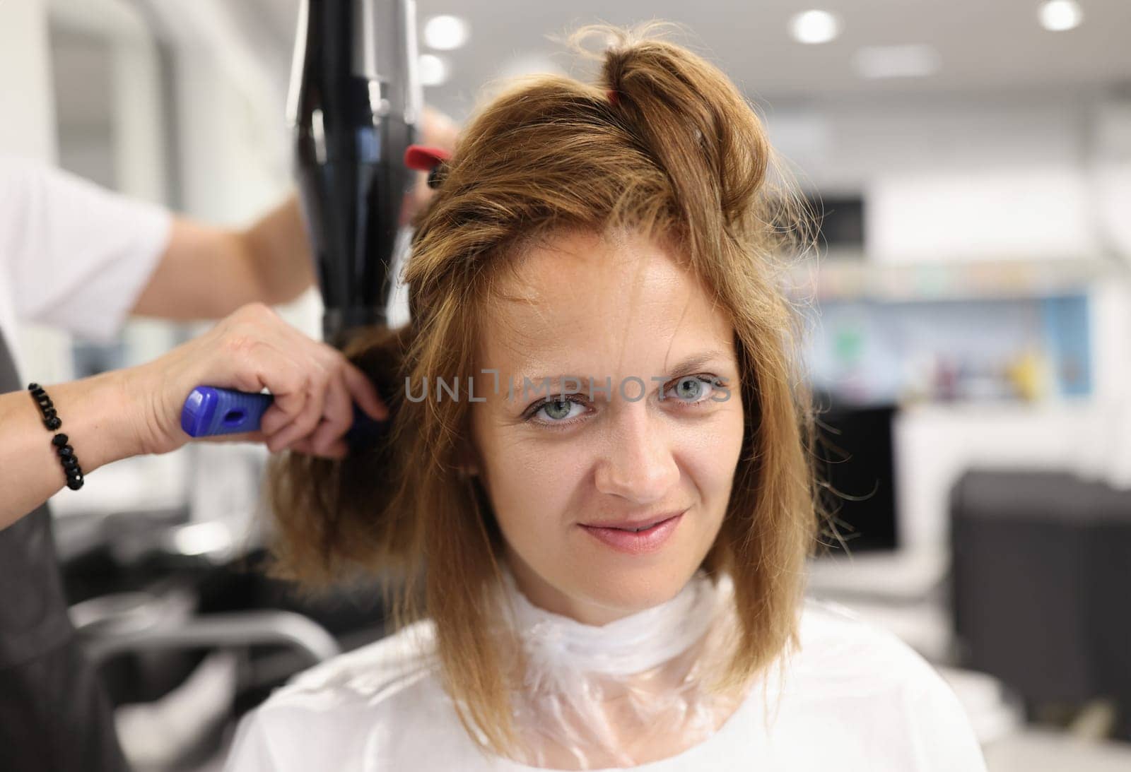 Woman hairdresser dries and straightens client hair with comb and hair dryer in beauty salon by kuprevich