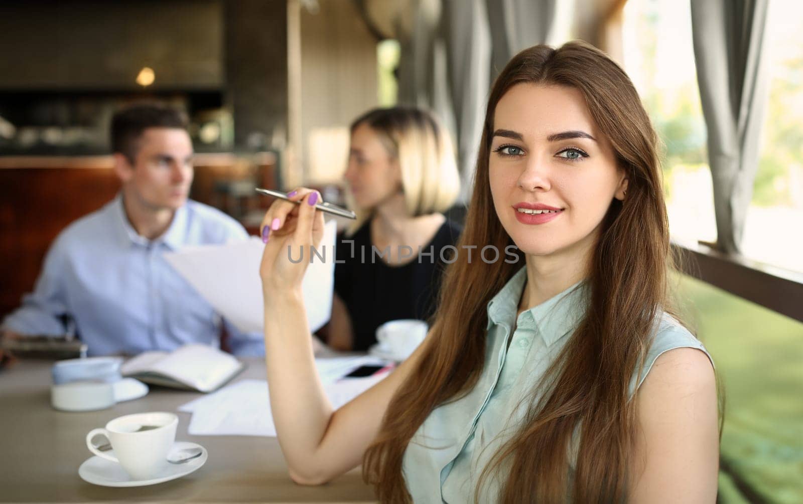 Portrait of a beautiful business woman sitting in cafe with colleagues discussing business project in background. Business meeting and discussion of business development