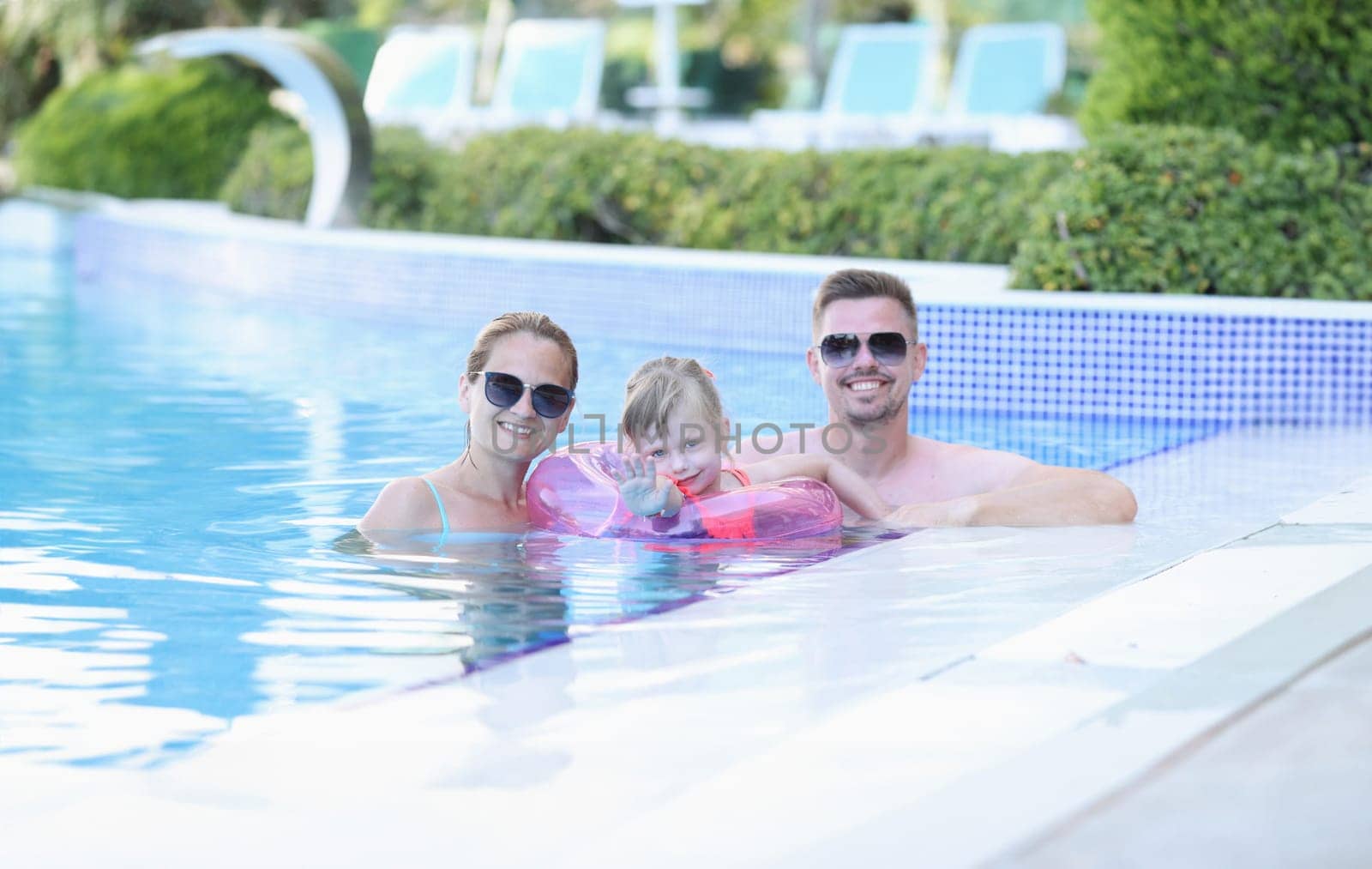 Portrait of young family with smiling child in pool. Happy joyful family together in pool