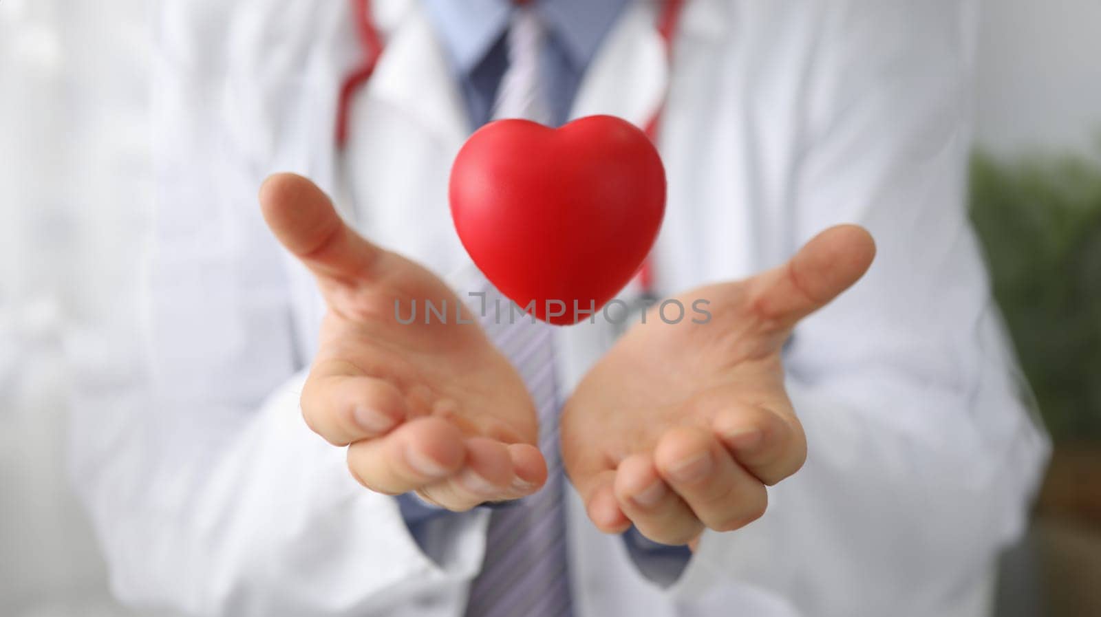 Doctor cardiologist holds hands and airborne red toy heart closeup. Cardiotherapist and treatment of heart diseases