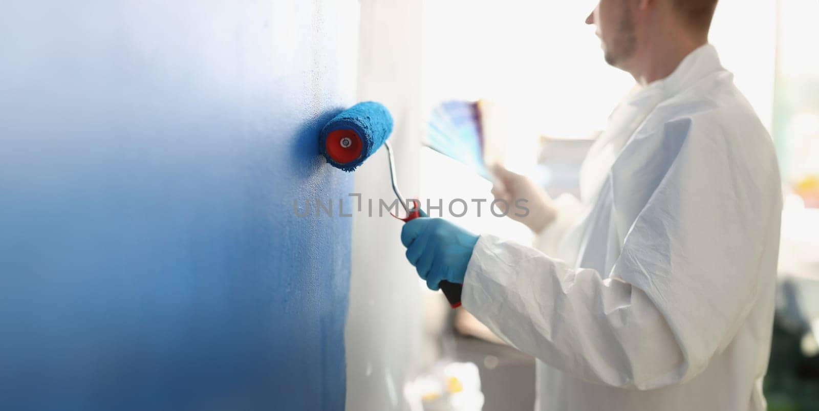Painting white wall with blue roller closeup by kuprevich