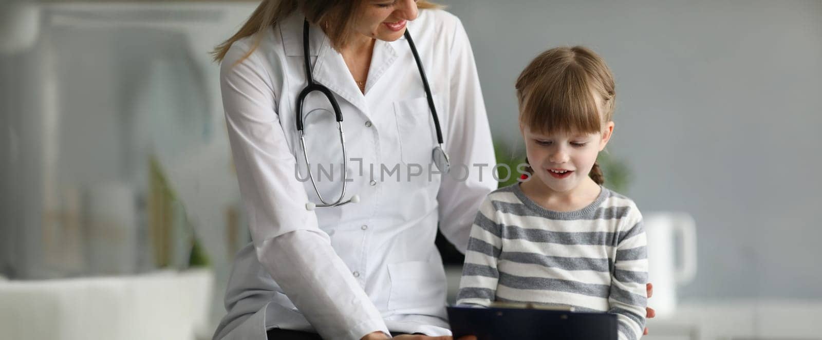 Little beautiful girl communicates with female doctor in clinic. Concept of children medical services and insurance