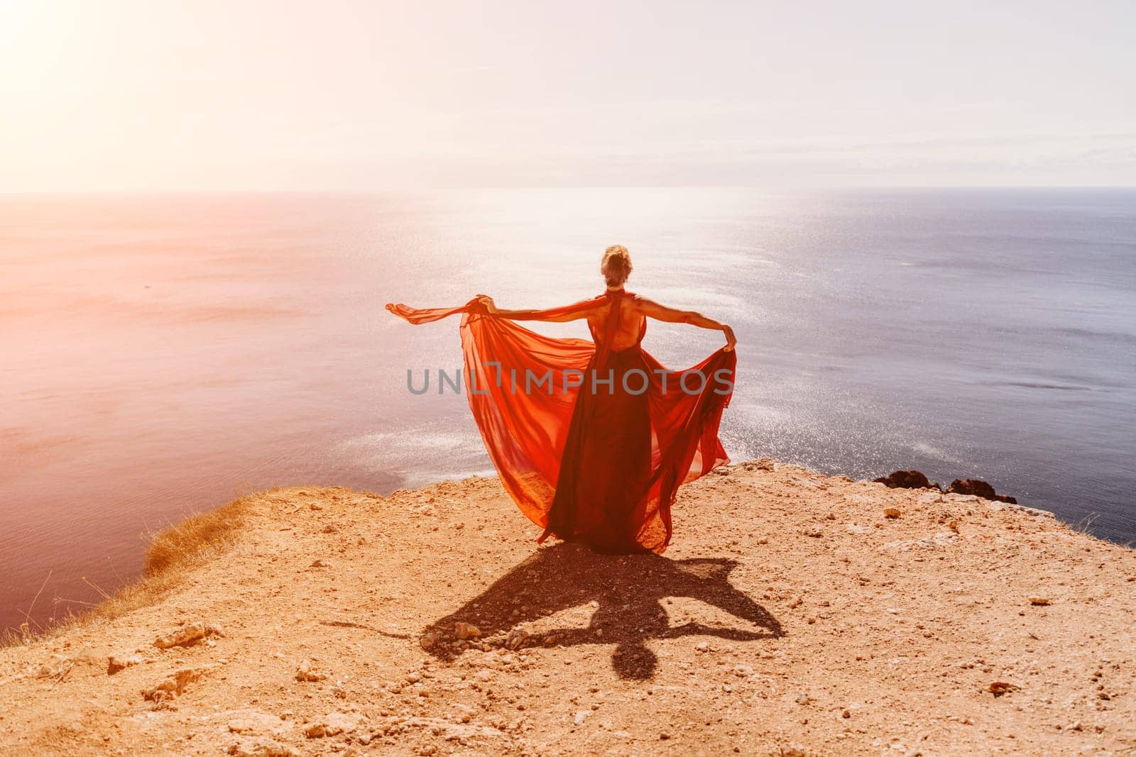 Woman red dress sea. Female dancer in a long red dress posing on a beach with rocks on sunny day. Girl on the nature on blue sky background