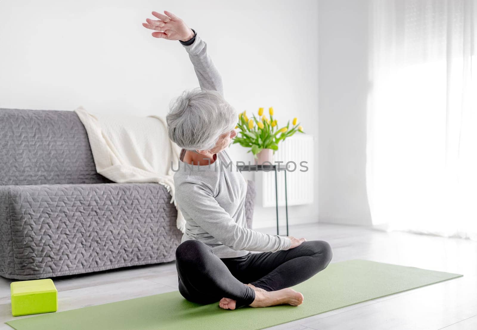 Calm Home Exercises In A Bright Room, A 70-Year-Old Woman Practices Yoga