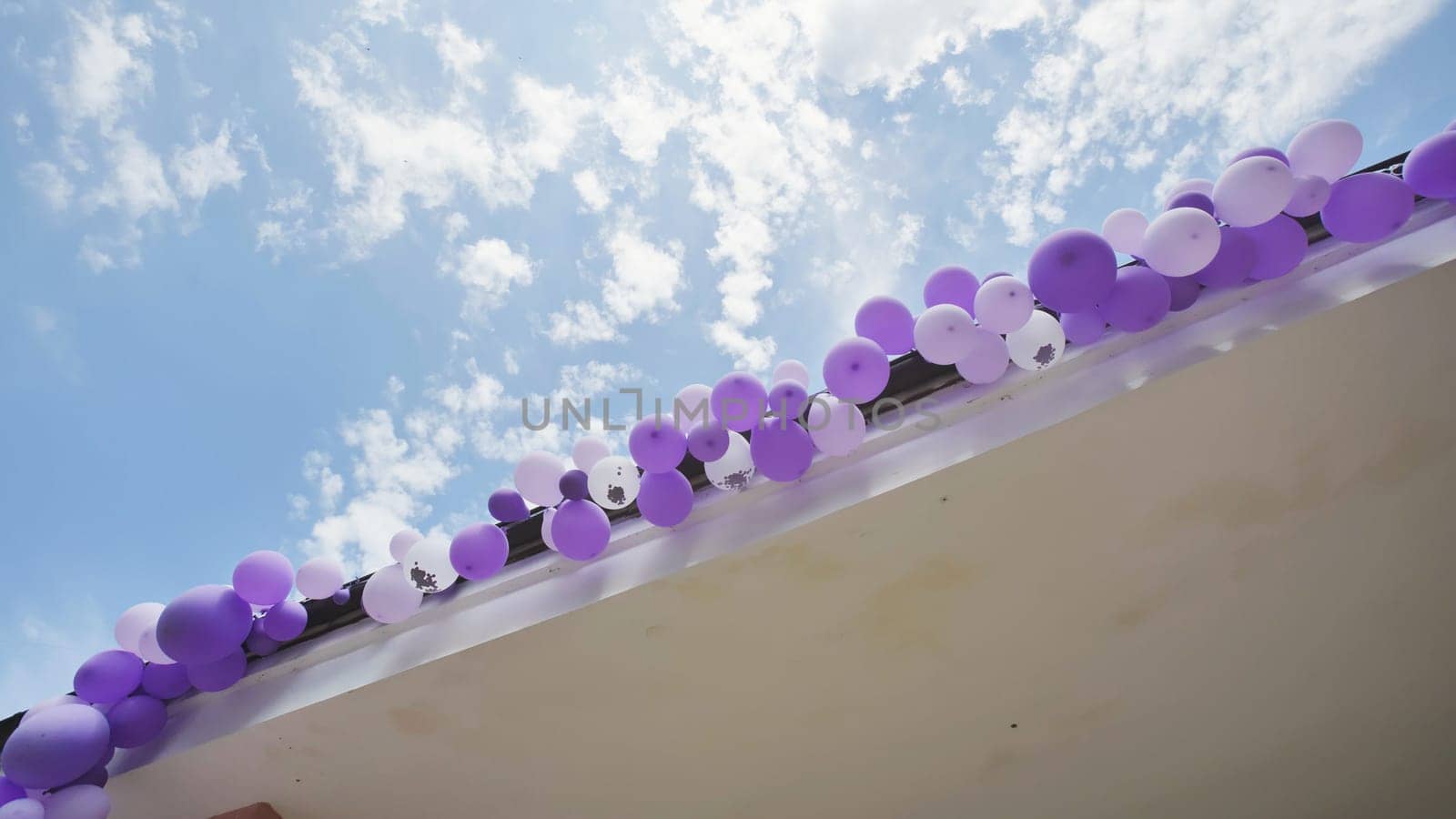 School rooftop adorned with purple and white balloons against a backdrop of a beautiful blue sky with clouds, marking the end of the school year