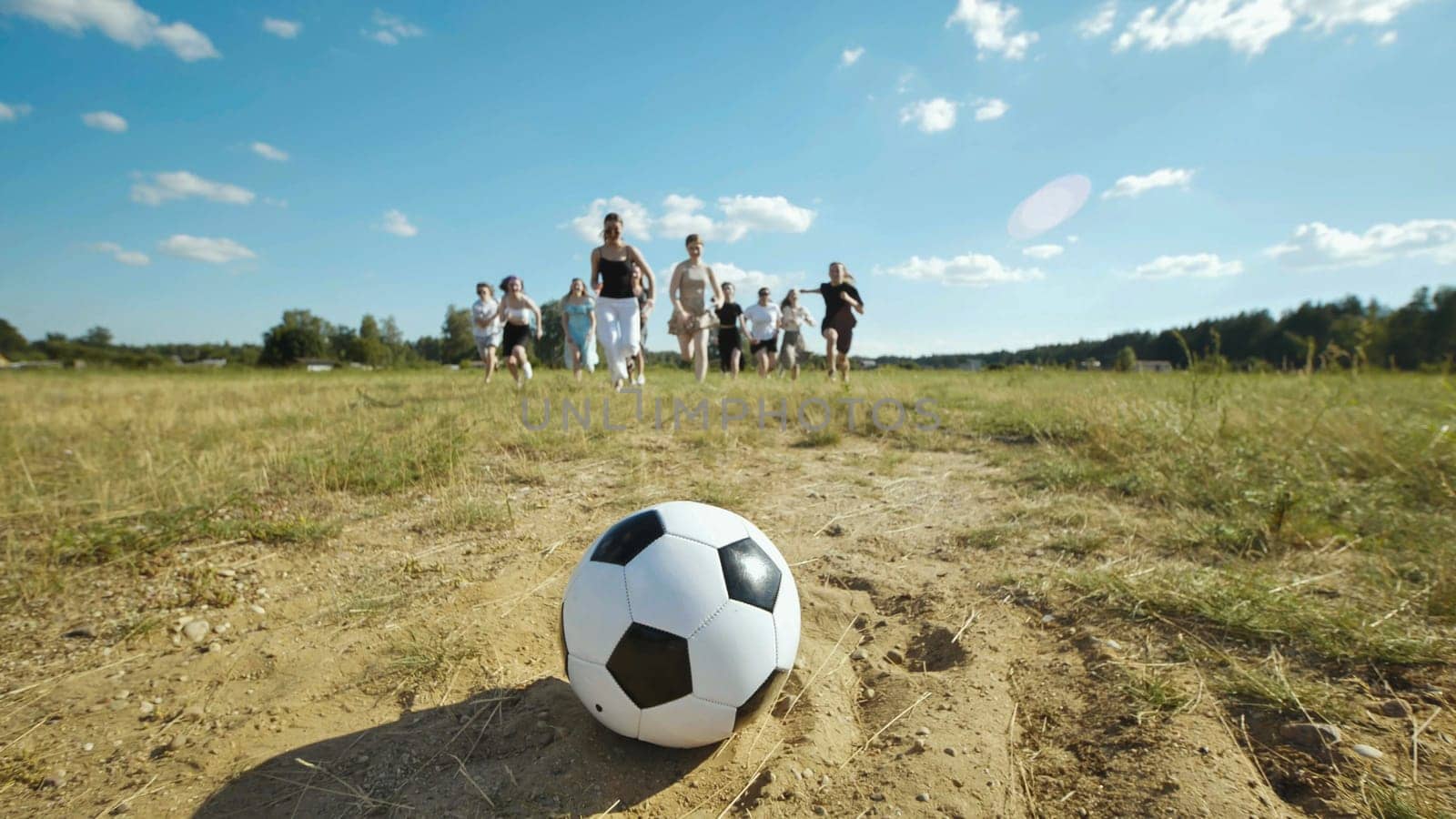 Group of high school students running towards a soccer ball during summer break in a grassy field