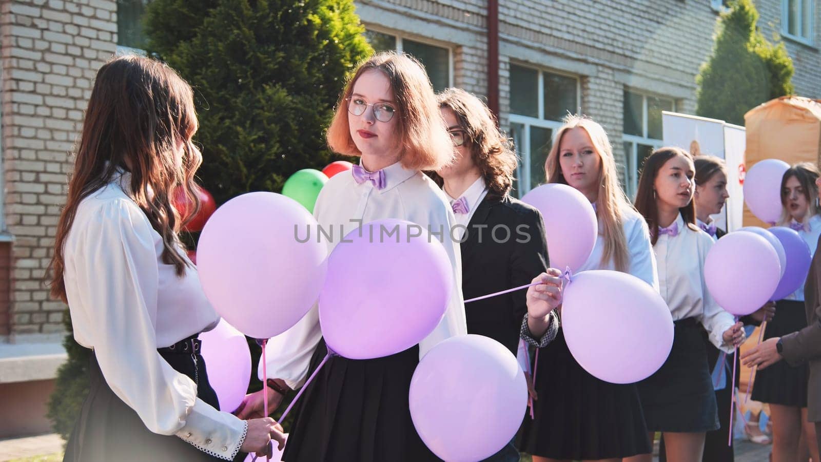 Female graduates in stylish attire celebrating their first day of school outdoors while holding purple balloons