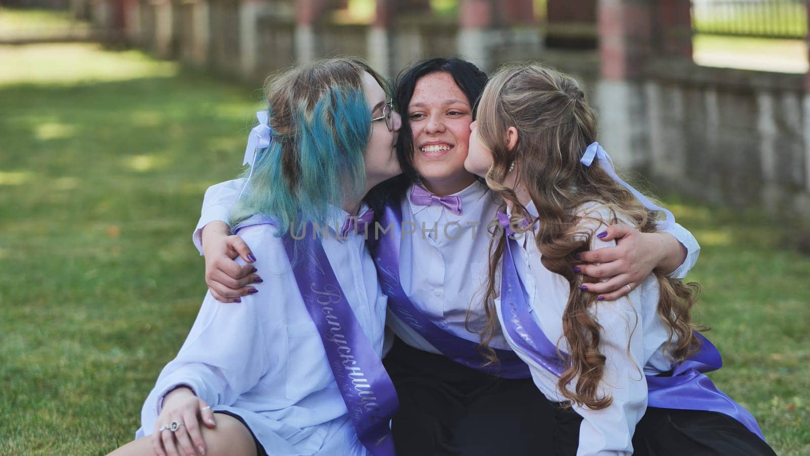 Three graduates celebrating their graduation by kissing their classmate on the cheeks during their last day of school