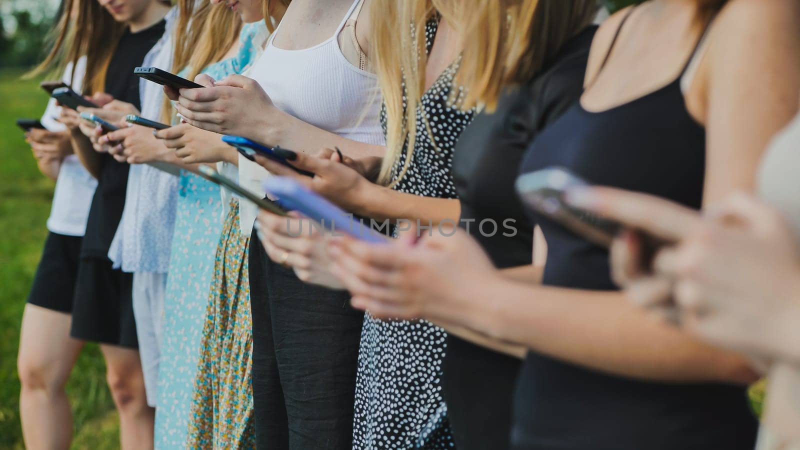 Group of students using smartphones outdoors in the summer, concept of technology addiction and social media
