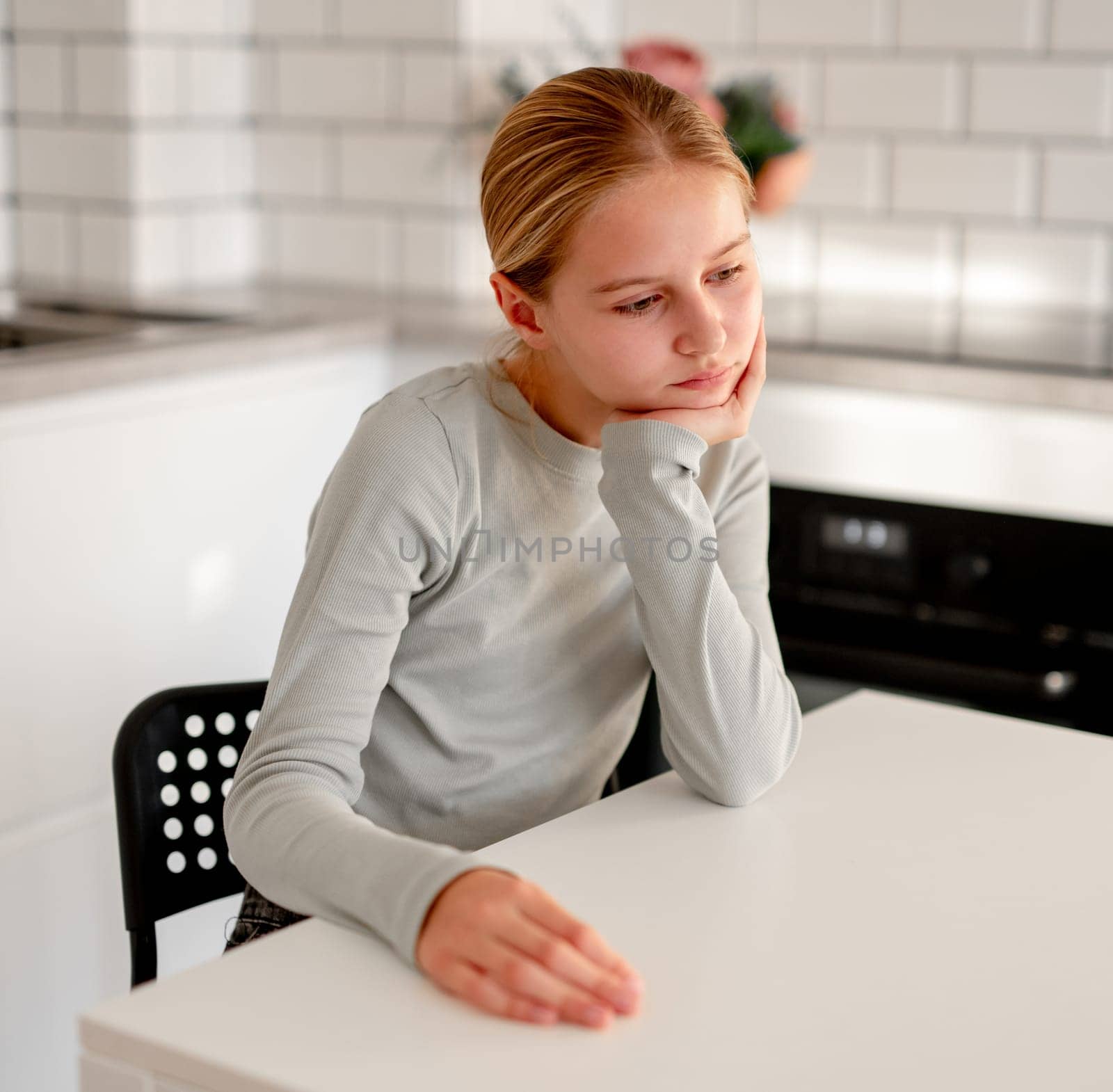 Cute Little Girl Sitting In The Kitchen At Home. It's Boring