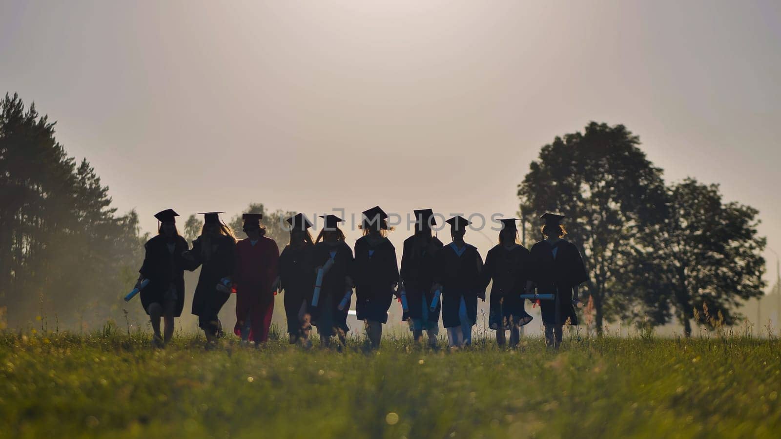 Six graduates in robes walk against the backdrop of the sunset.