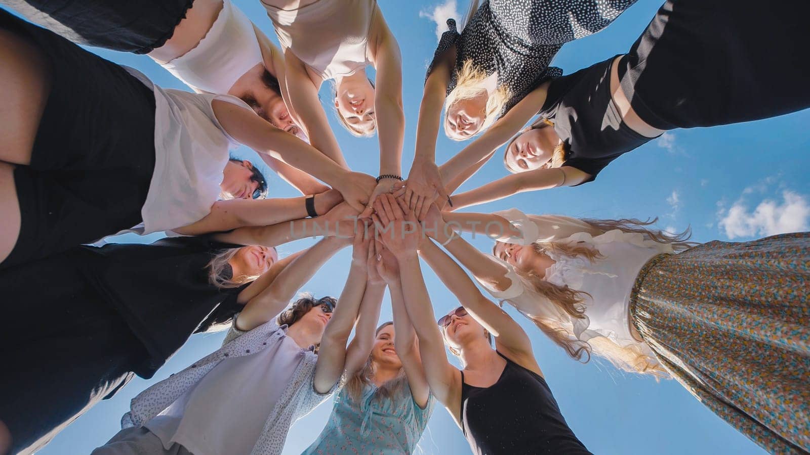 Group of high school students forming a circle, joining their hands together against a bright blue sky, symbolizing teamwork, unity, and collaboration