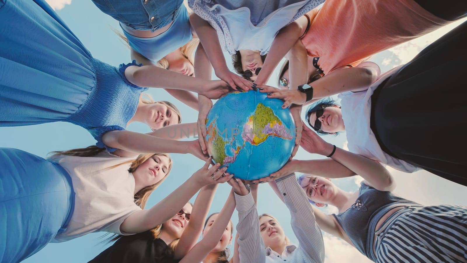 Earth conservation concept. 10 girls and boys surround the rotating earth globe with their palms. A view in motion