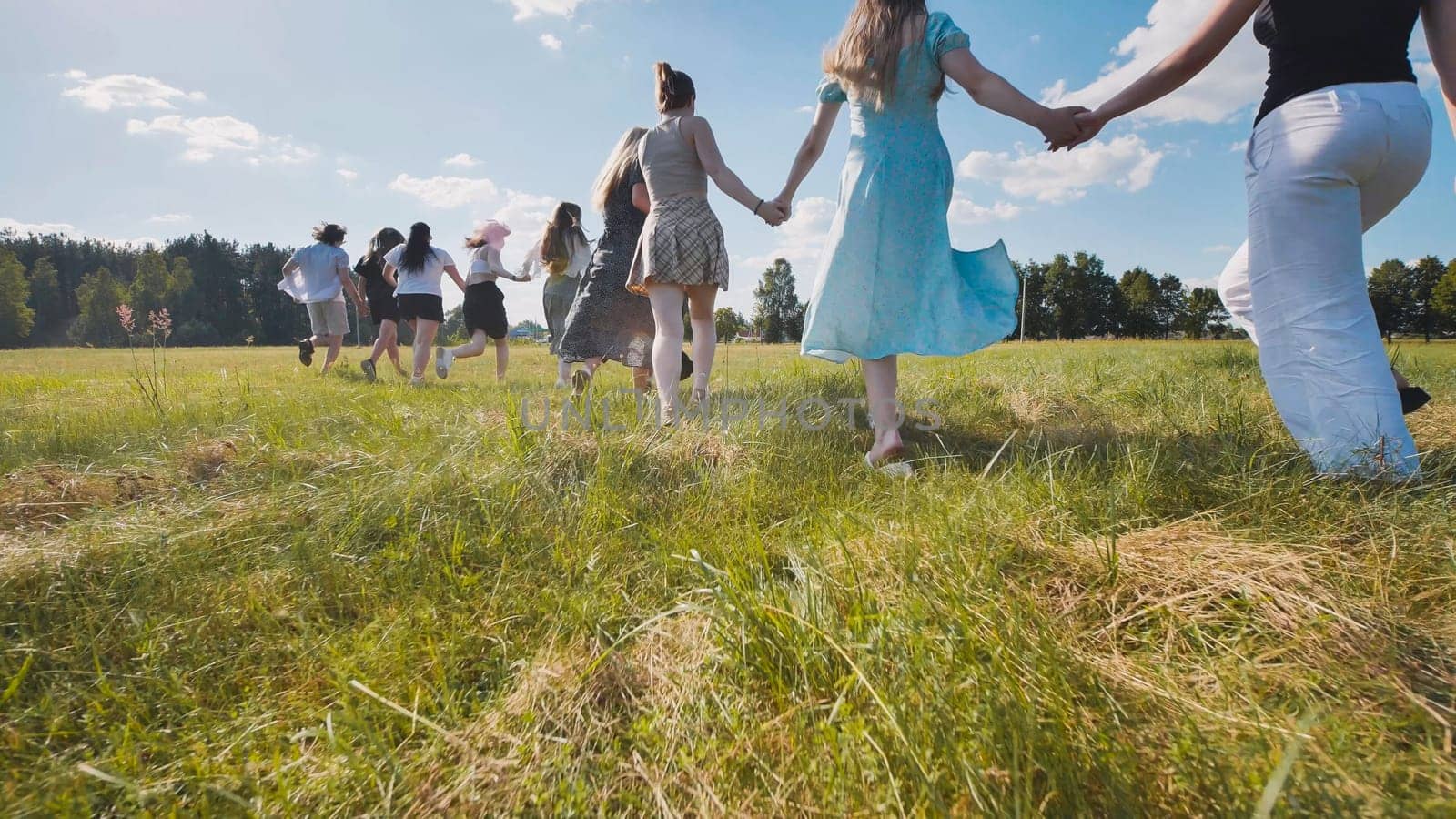 Group of high school students holding hands running through meadow celebrating end of school year in summer