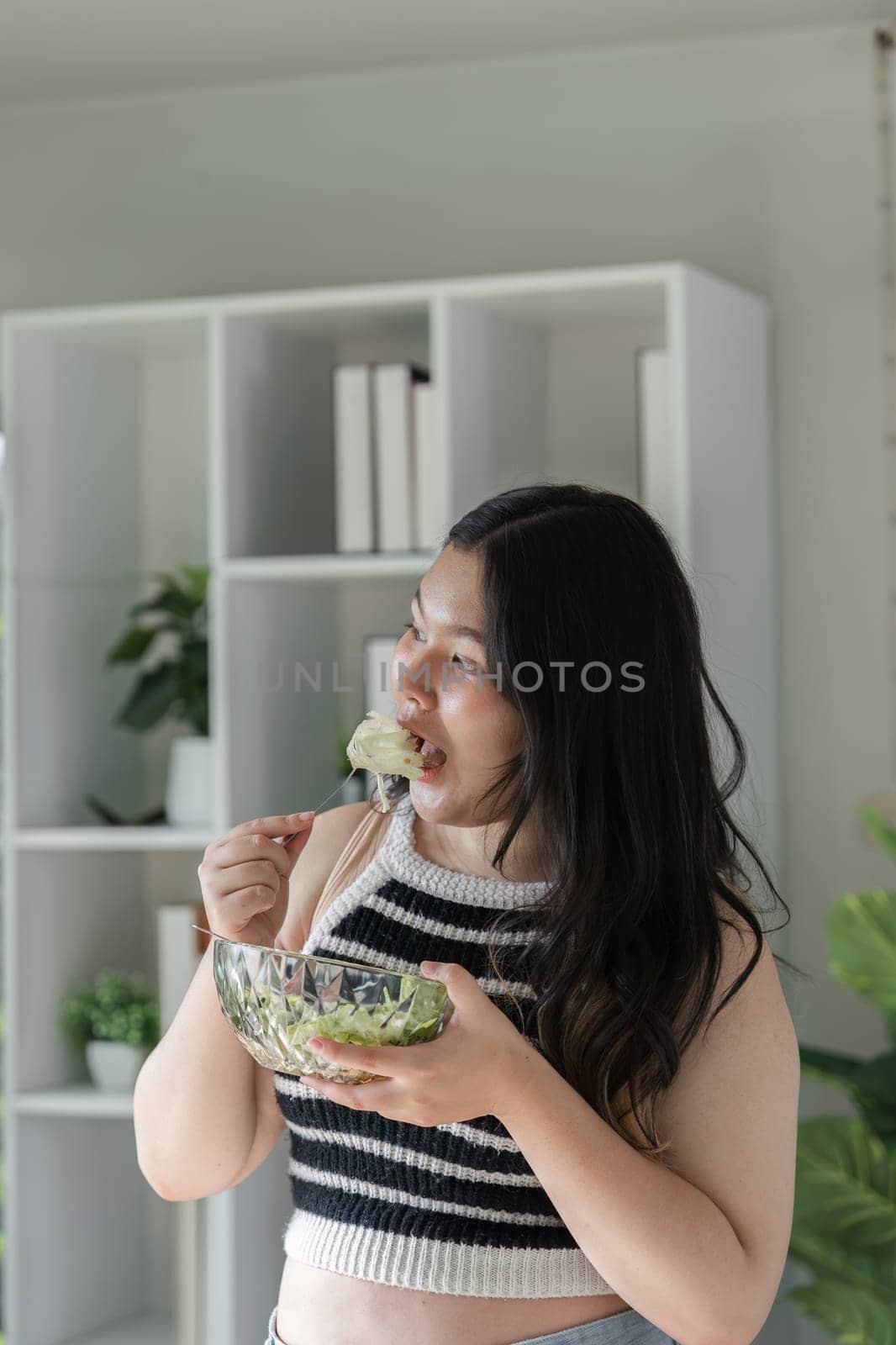 A woman happily eating a nutritious salad, promoting healthy eating habits in a contemporary home environment.