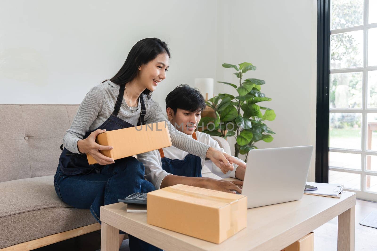 A couple working together in a modern living room, taking online orders and packing products for their e-commerce business.