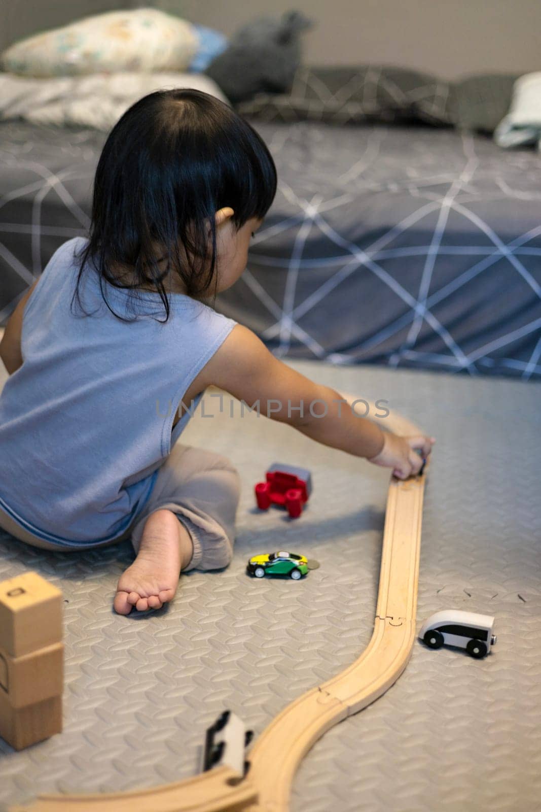 Little boy in a blue shirt sits on the floor playing with a blue train on a wooden track. Education concept.