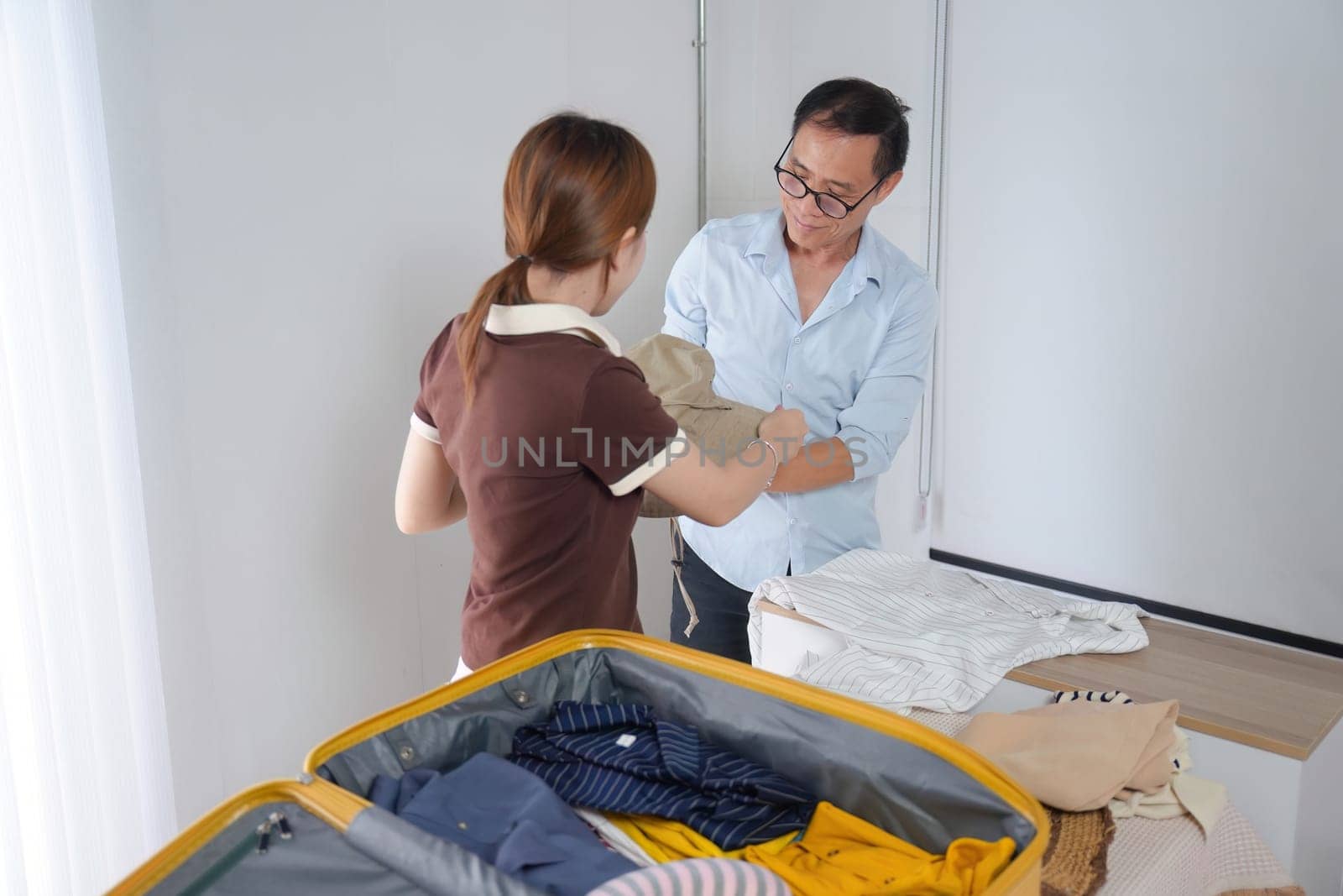 A father and daughter enjoy quality time together as they fold clothes and pack a suitcase, preparing for a family vacation.