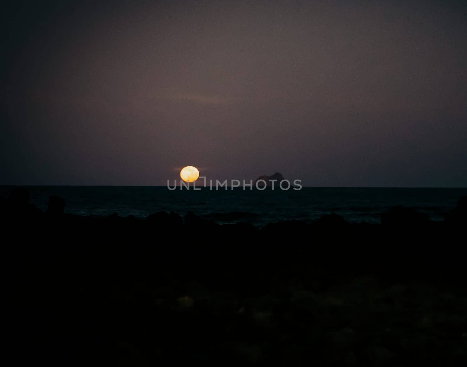 Early sunrise or sunset over the ocean, beach with black volcanic sand at dusk in the darkness the first ray.