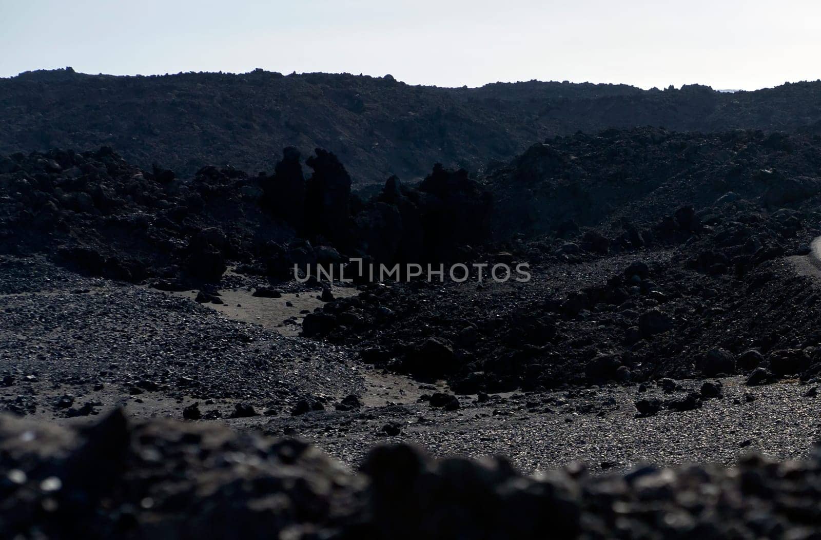 Harsh dramatic volcanic dark soil, lifeless desert with black lava formations and basalt rocks at the foot of the volcano without people.