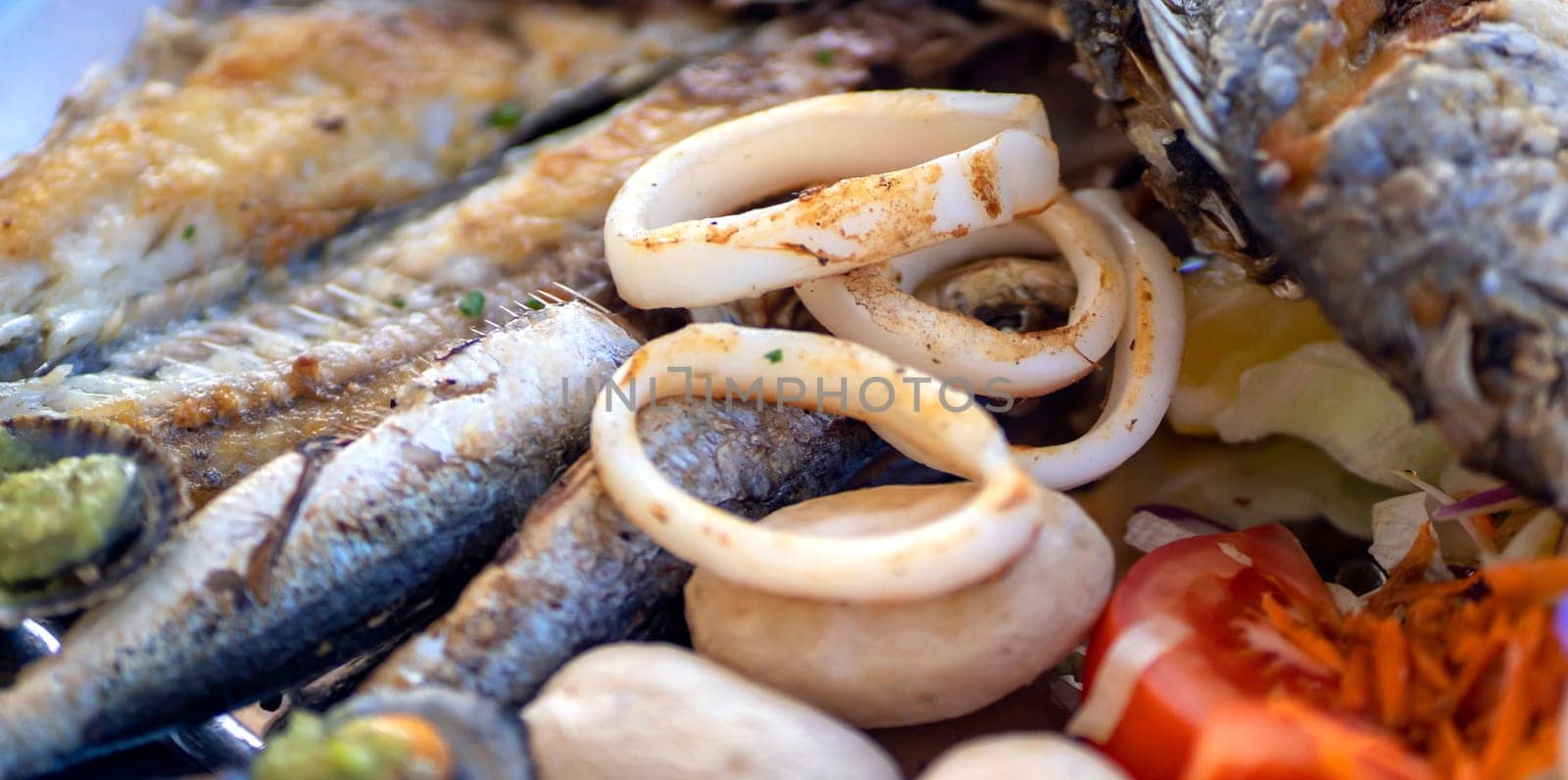 Delicious grilled fish mix plate, a dish with different types of fish, sardines, salmon and seafood, scallops, squid rings from an Atlantic Ocean served in a restaurant in the Canary Islands.
