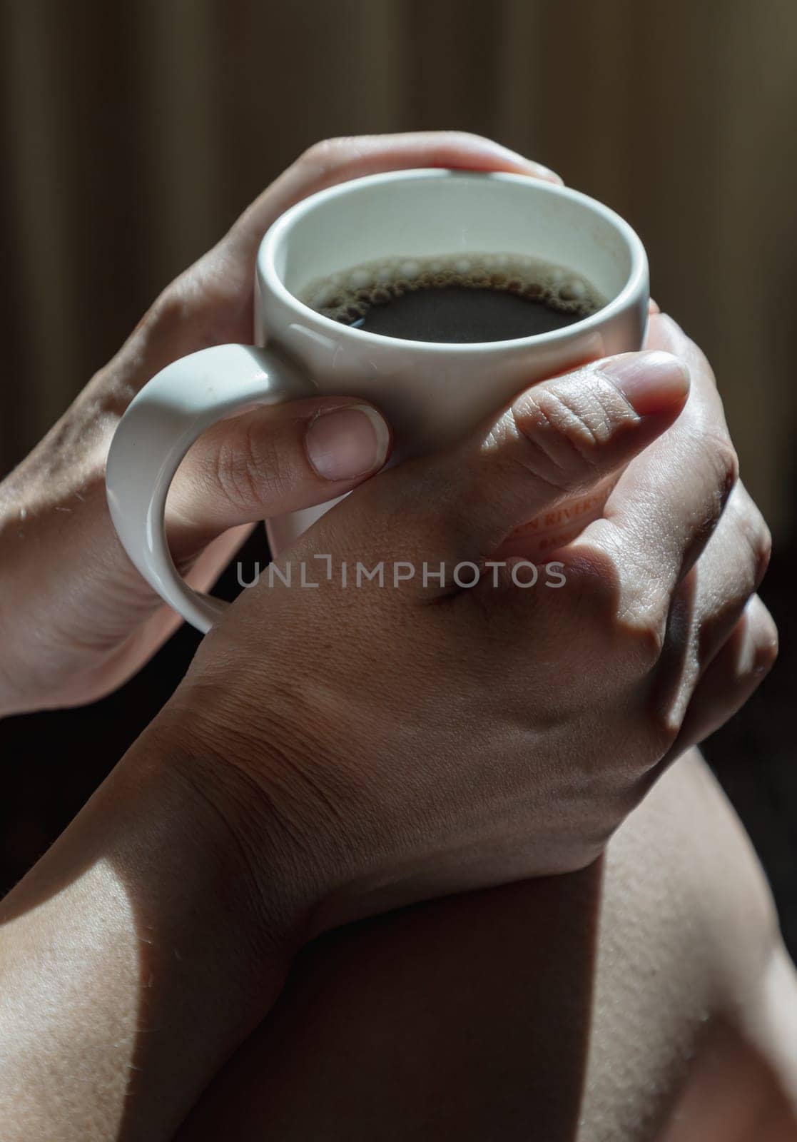 Close-up of Comforting cozy female hands holding a coffee mug with the morning sunlight that shines through. Dark tone, use it as your Wallpaper, Poster and Copy space, Selective focus.