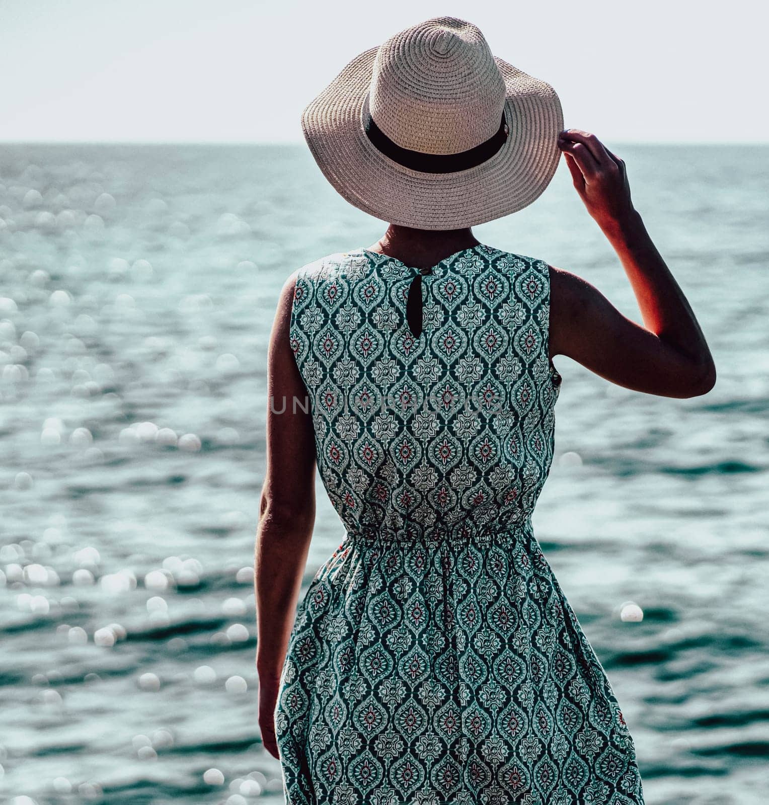 A young graceful girl in an elegant light blue dress with ornaments stands and looks at the endless ocean, a lady in a hat enjoys a vacation at sea, happily spends her leisure time during holidays.